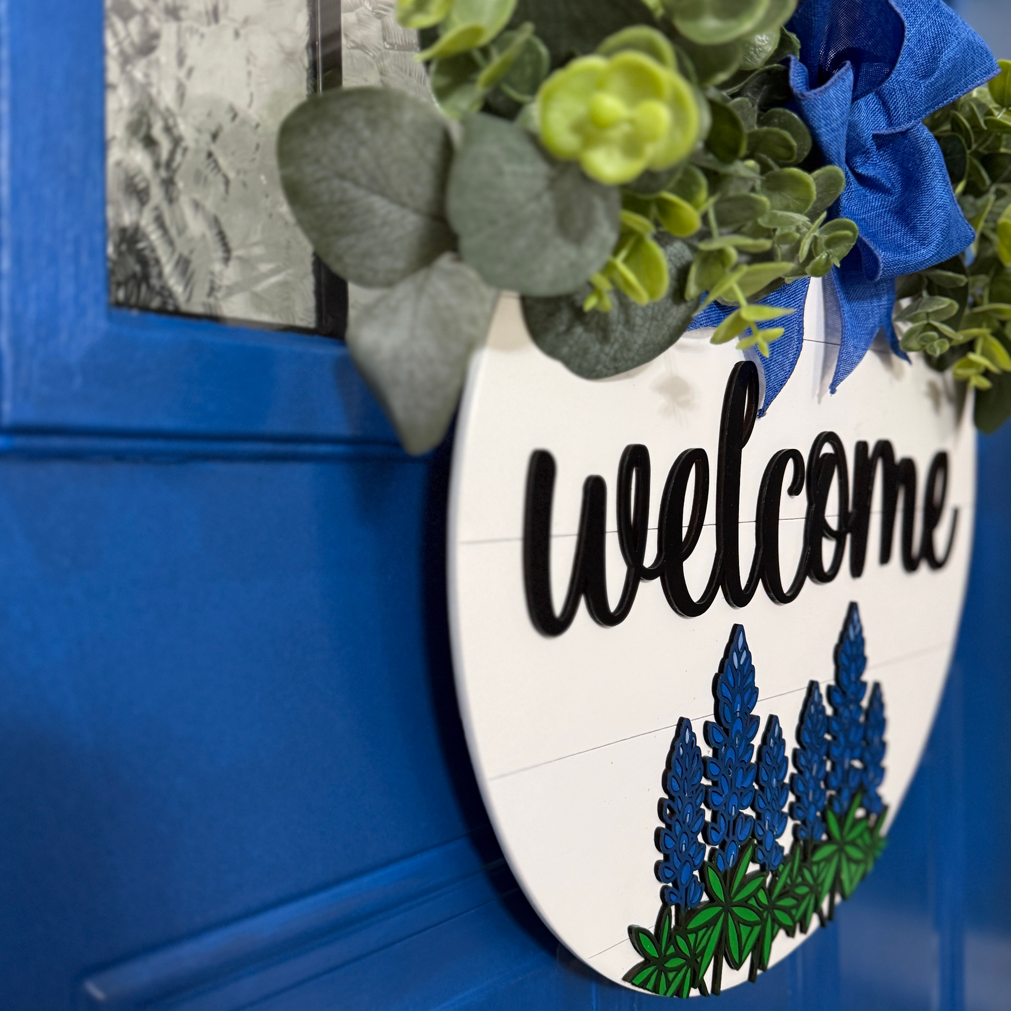 Hand-painted bluebonnet welcome sign hanging on bright blue front door