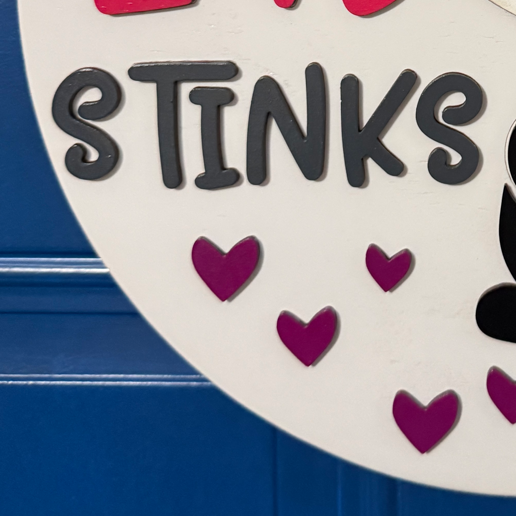 Close-up of black Stinks lettering with pink and purple hearts on Valentine door hanger
