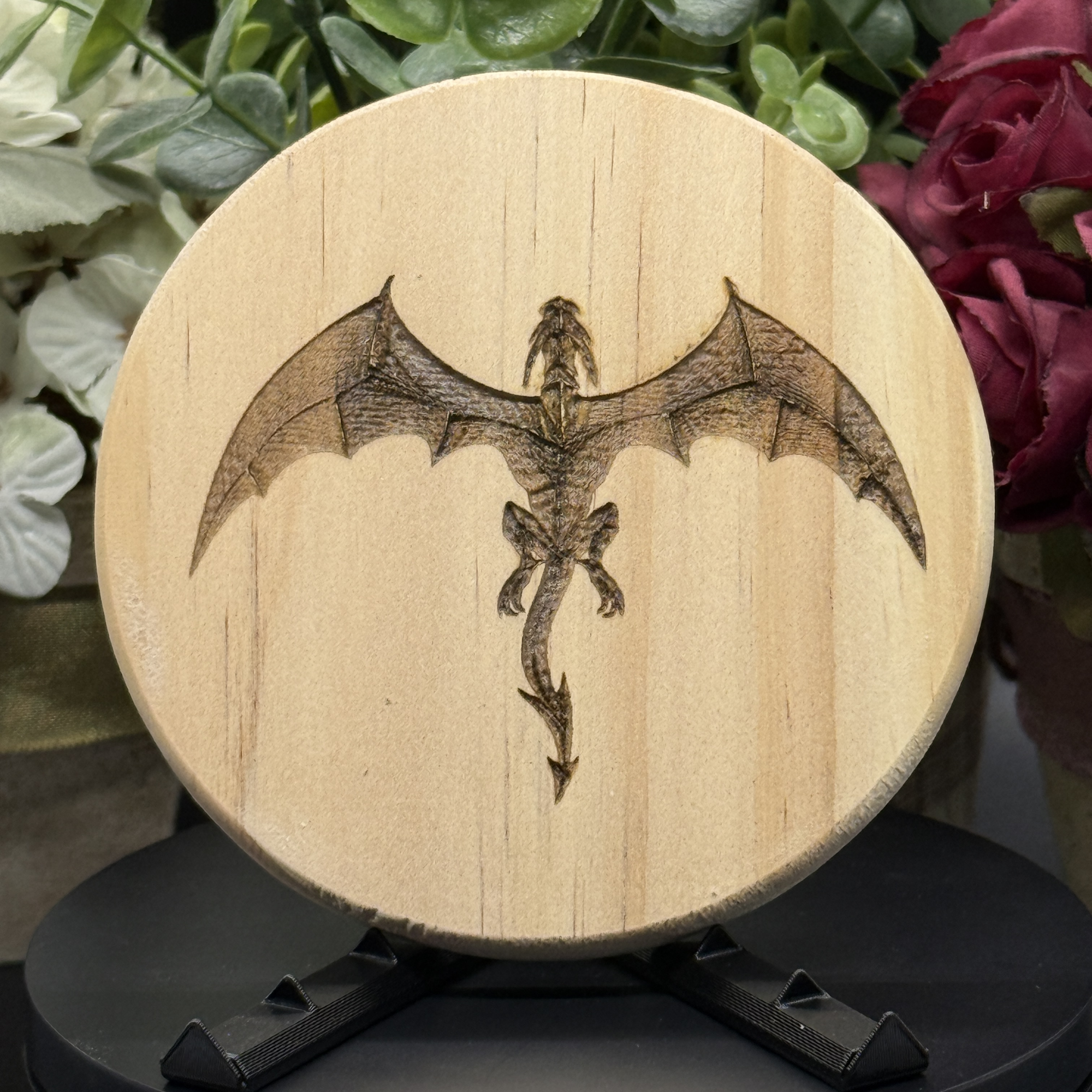 Round pine wood coaster with top-down view of a flying dragon with extended wings, laser-engraved in fine detail