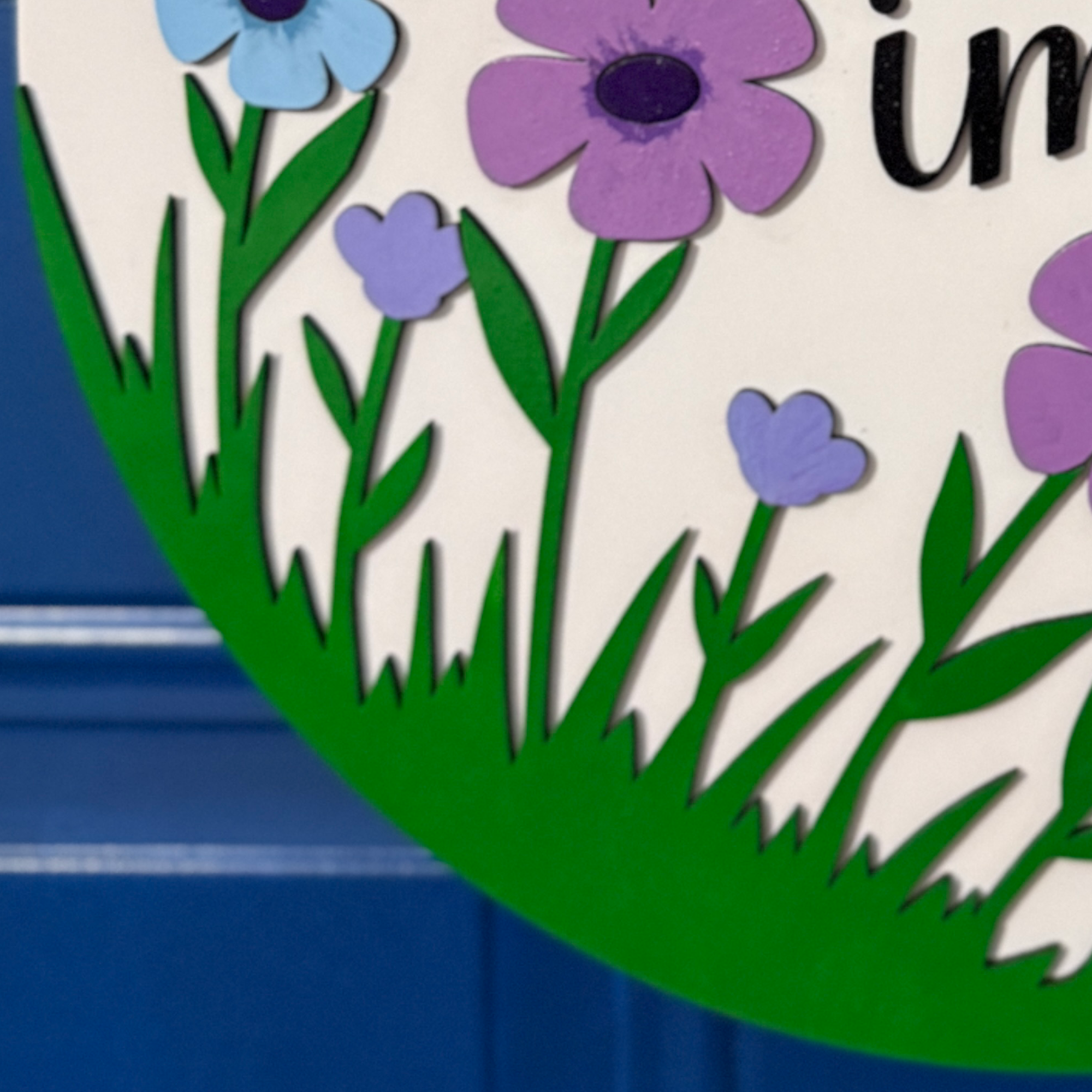 Close-up of lower section showing green grass and layered purple flowers on round wood sign