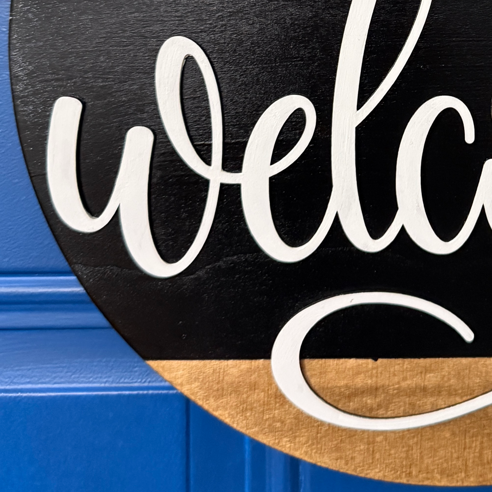 Close up of Welcome door hanger on stained base with black background, faux with greenery and coordinating bow