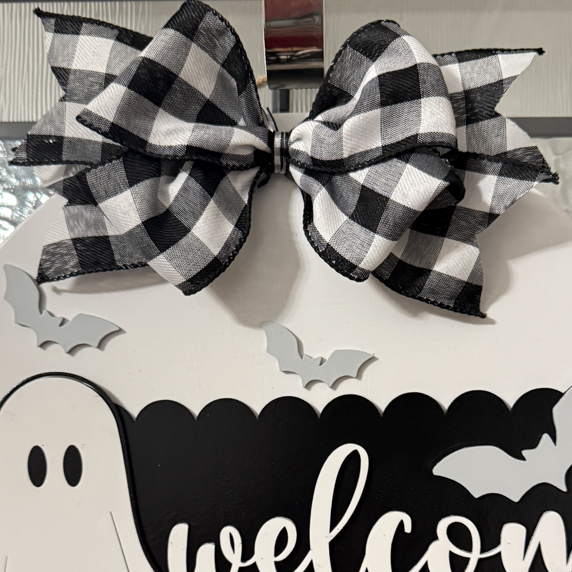 Close-up view of Halloween door hanger highlighting ghost graphic, bats, and buffalo plaid bow