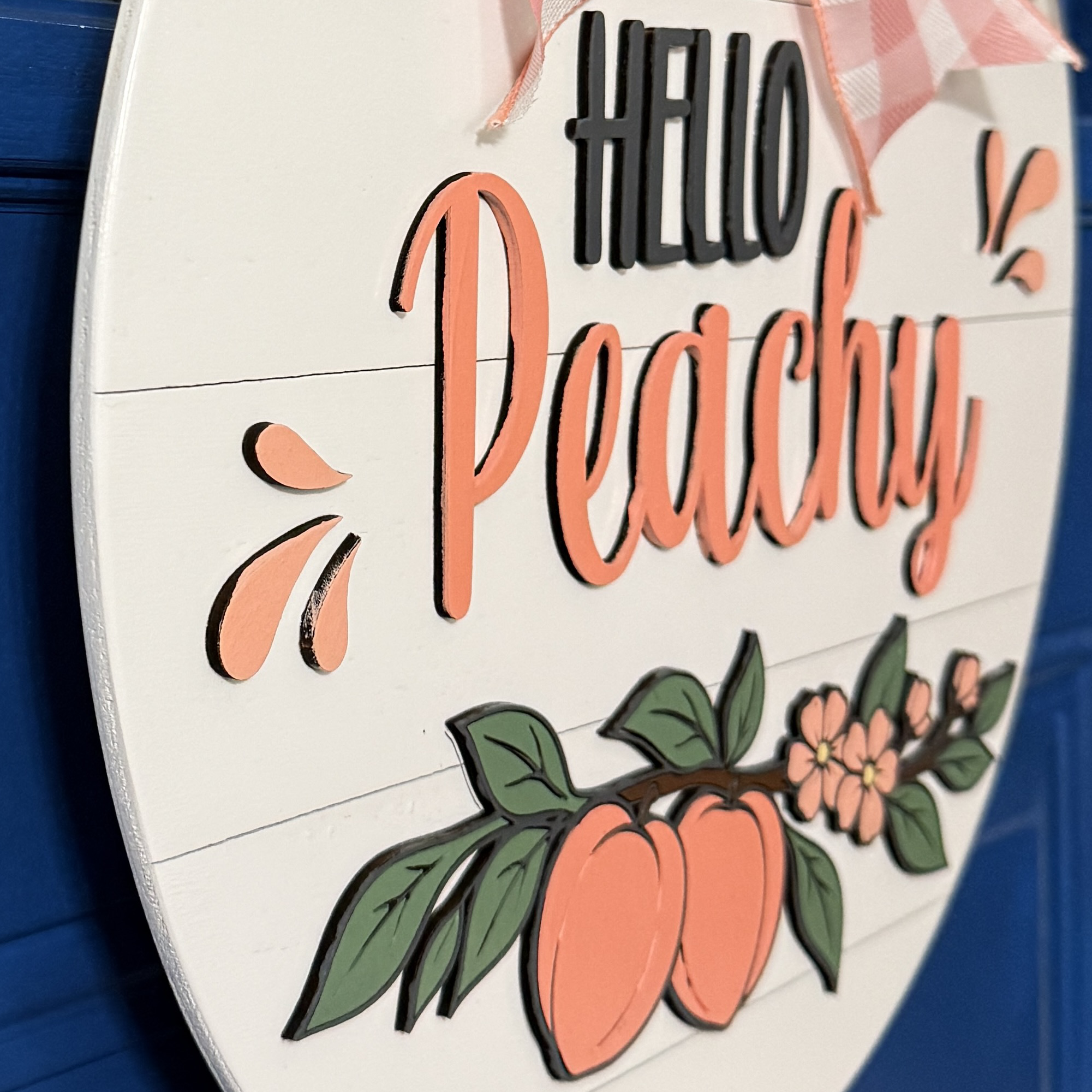 Side angle view of dimensional Hello Peachy lettering and peach illustration on layered wood door hanger