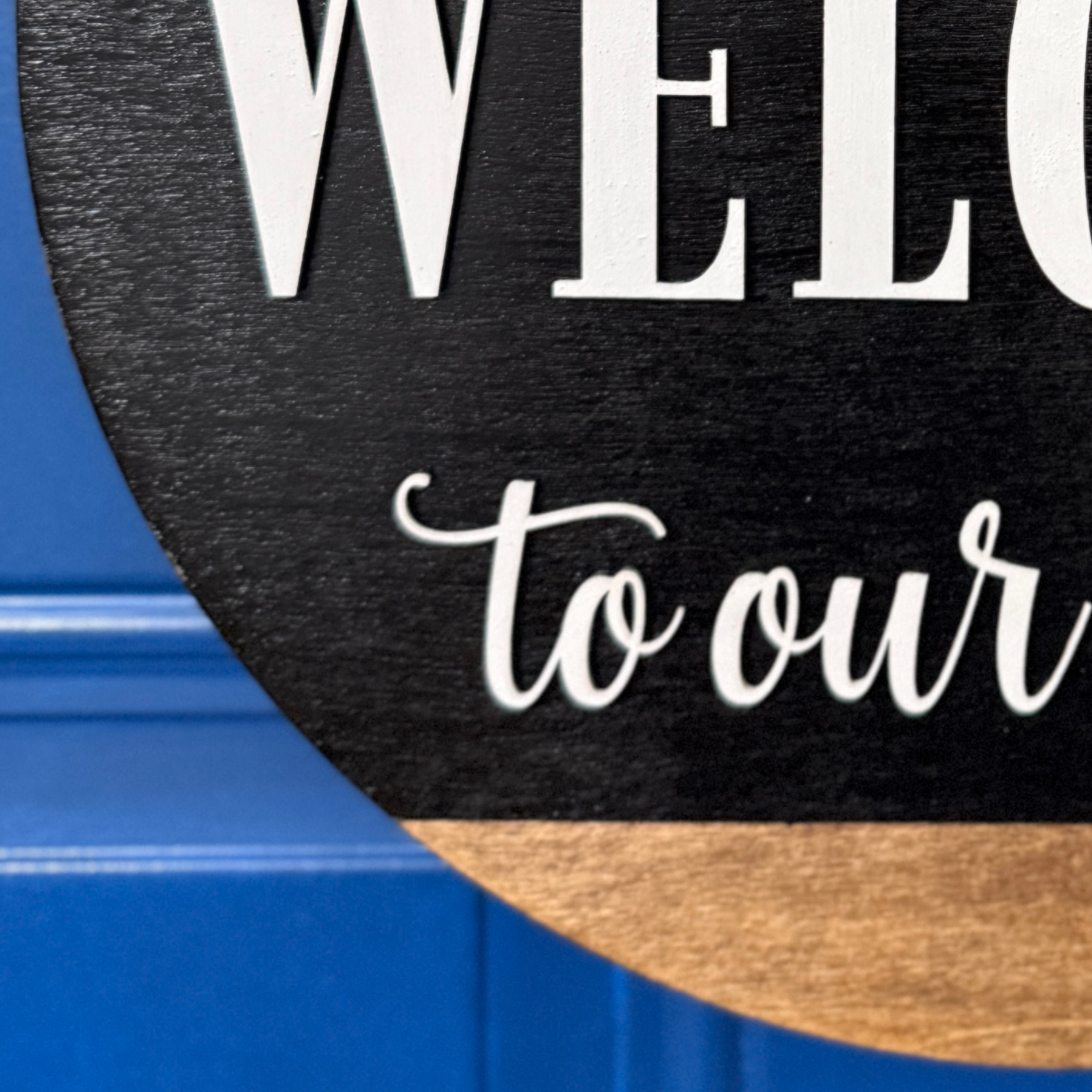 Close-up of white welcome to our home lettering on black painted wood door hanger with natural wood accent