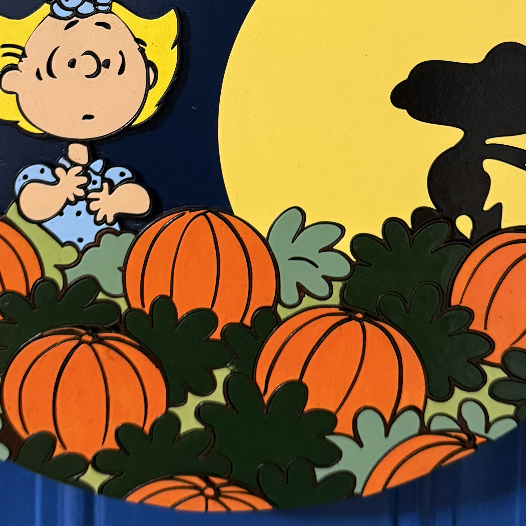 Close-up of Peanuts characters Linus and Sally among pumpkins with stars and Snoopy’s moonlit silhouette