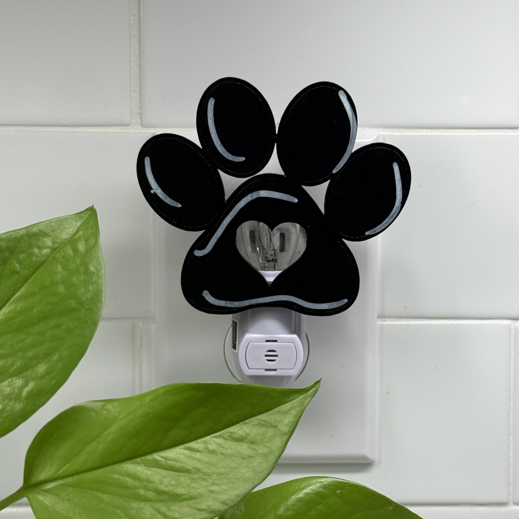 Black paw print night light with heart cutout, unplugged and shown in daylight on tiled wall