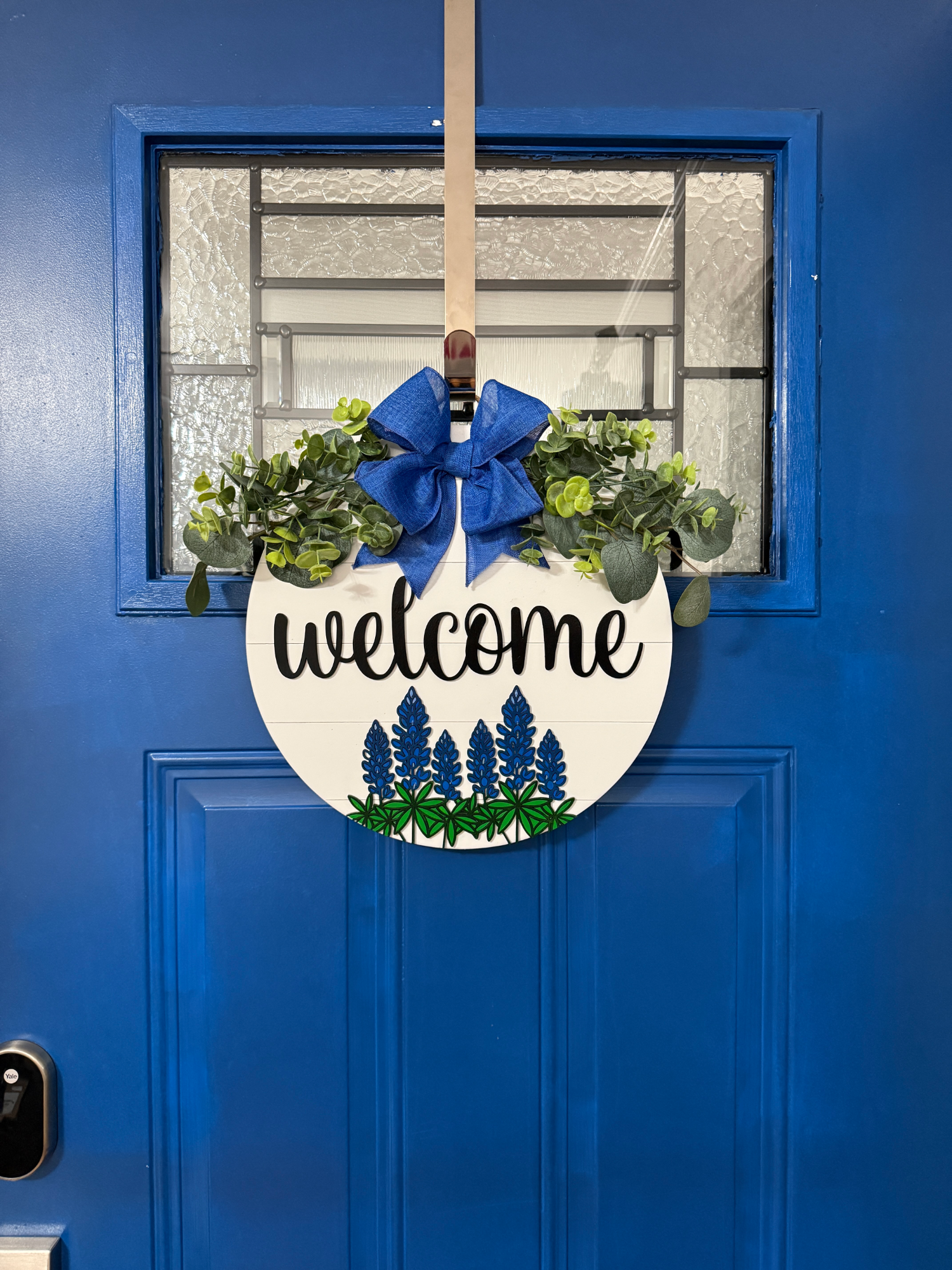 White shiplap welcome sign with blue flowers displayed on front door
