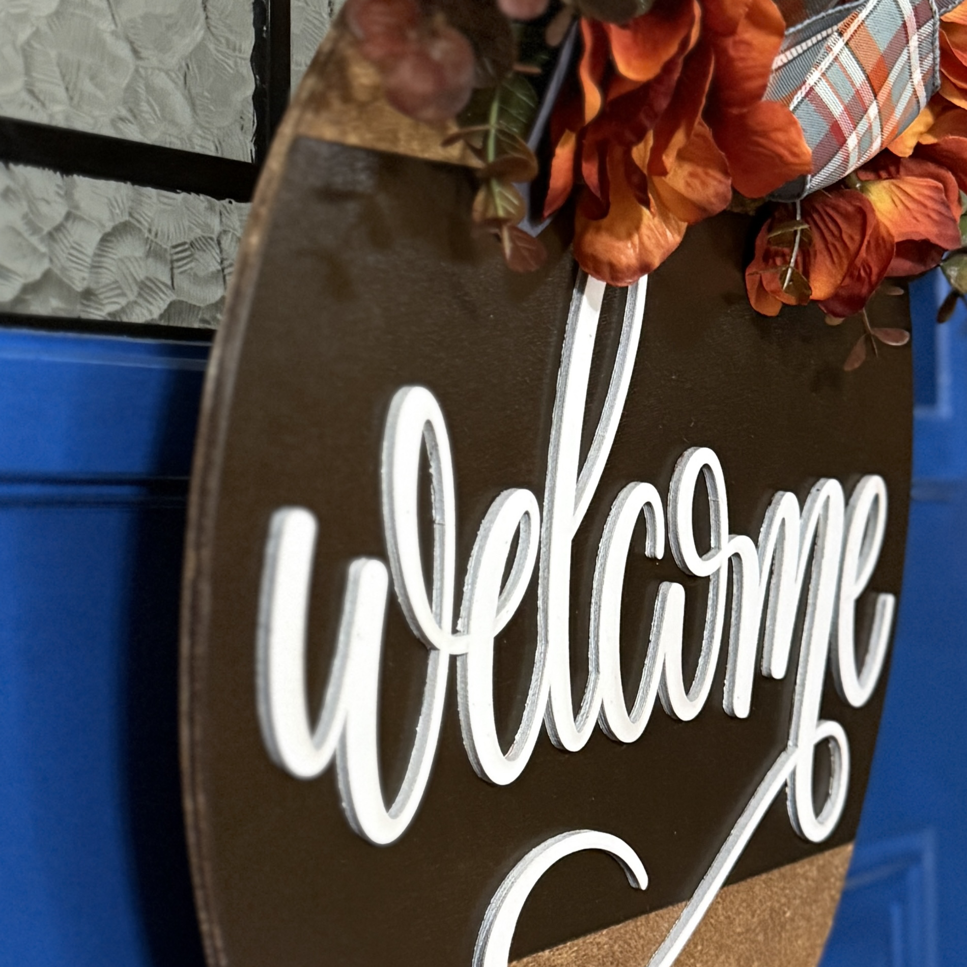 Close-up of “welcome” lettering and layered floral accents on autumn door hanger