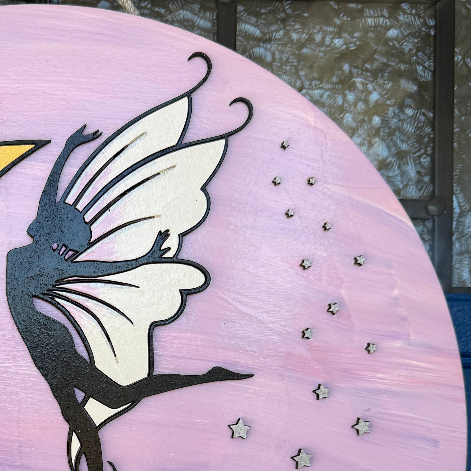 Close-up of black fairy silhouette with white wings and star accents on pink background door hanger