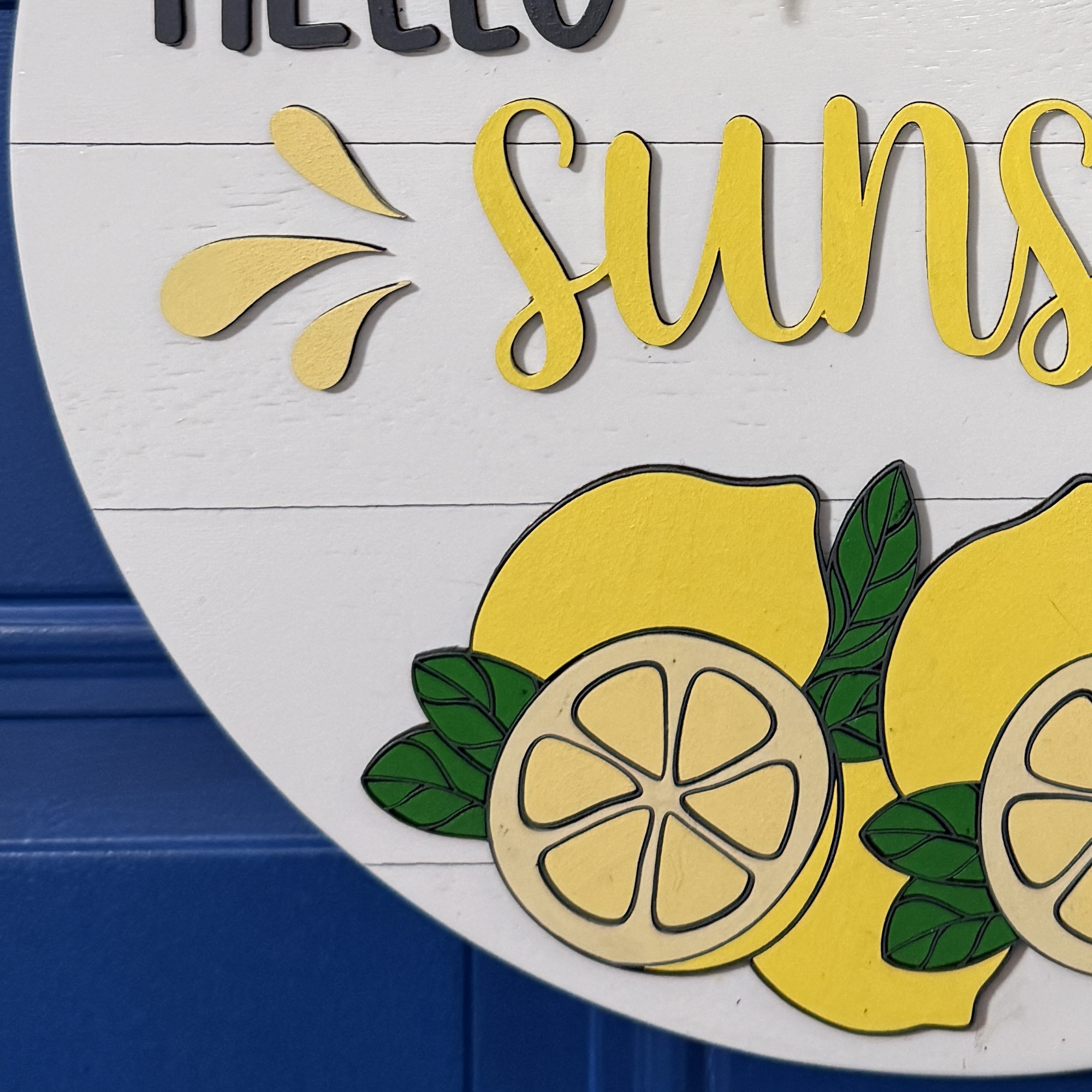 Close-up of hand-painted whole and sliced lemons with green leaves on round wood door hanger