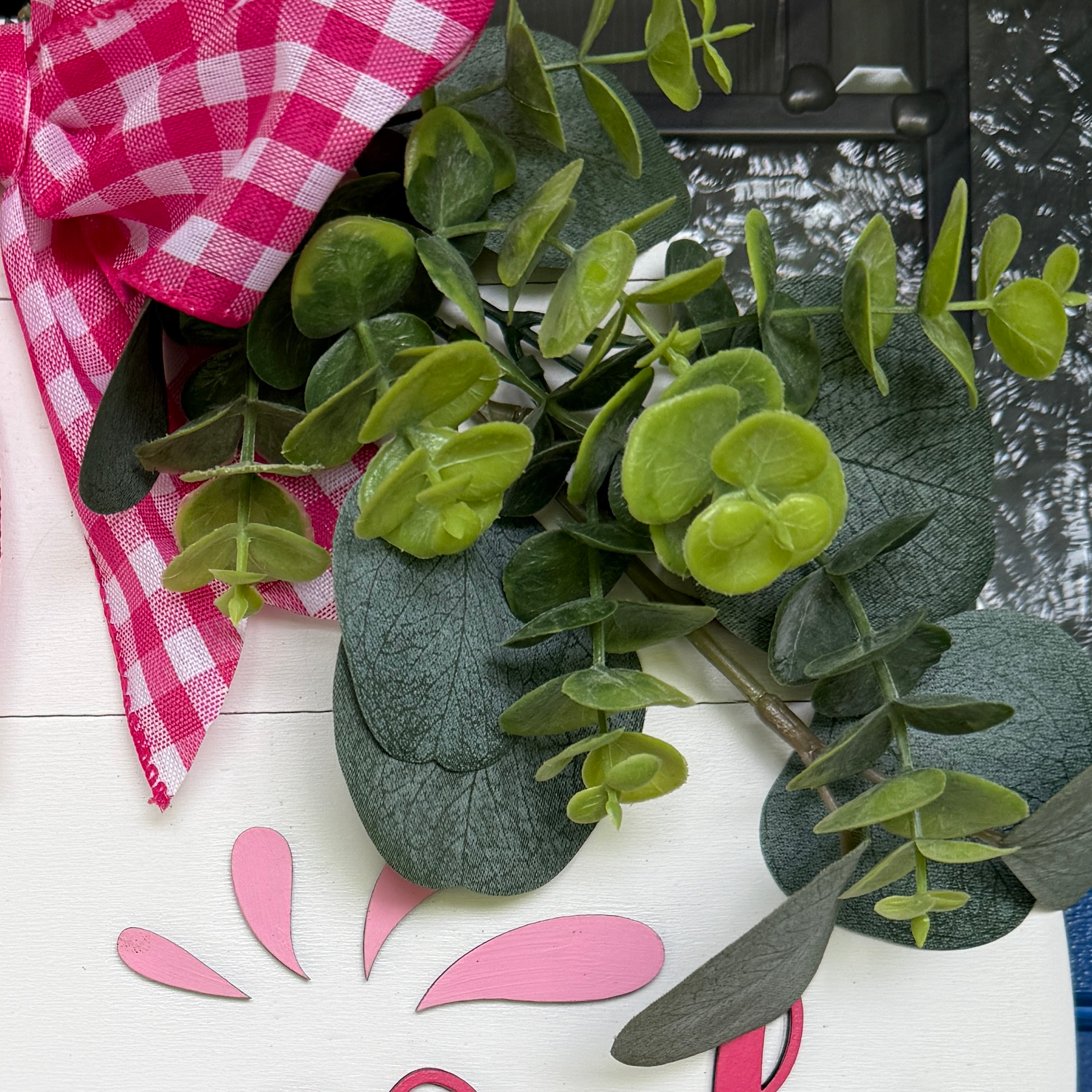 Detail view of eucalyptus greenery and decorative flourish accents on a handcrafted watermelon door hanger.