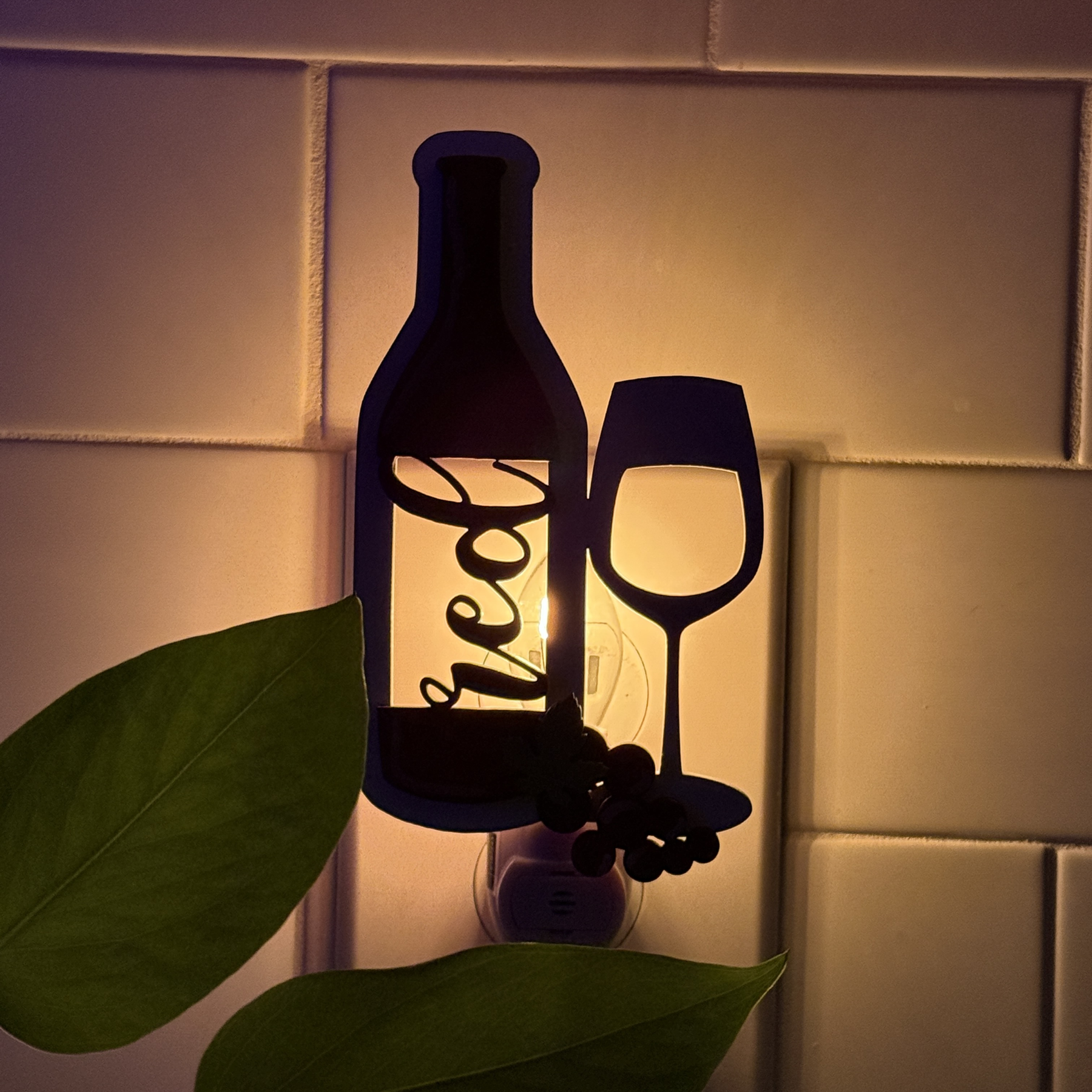 Glowing red wine bottle and glass night light plugged in, dark kitchen tile background