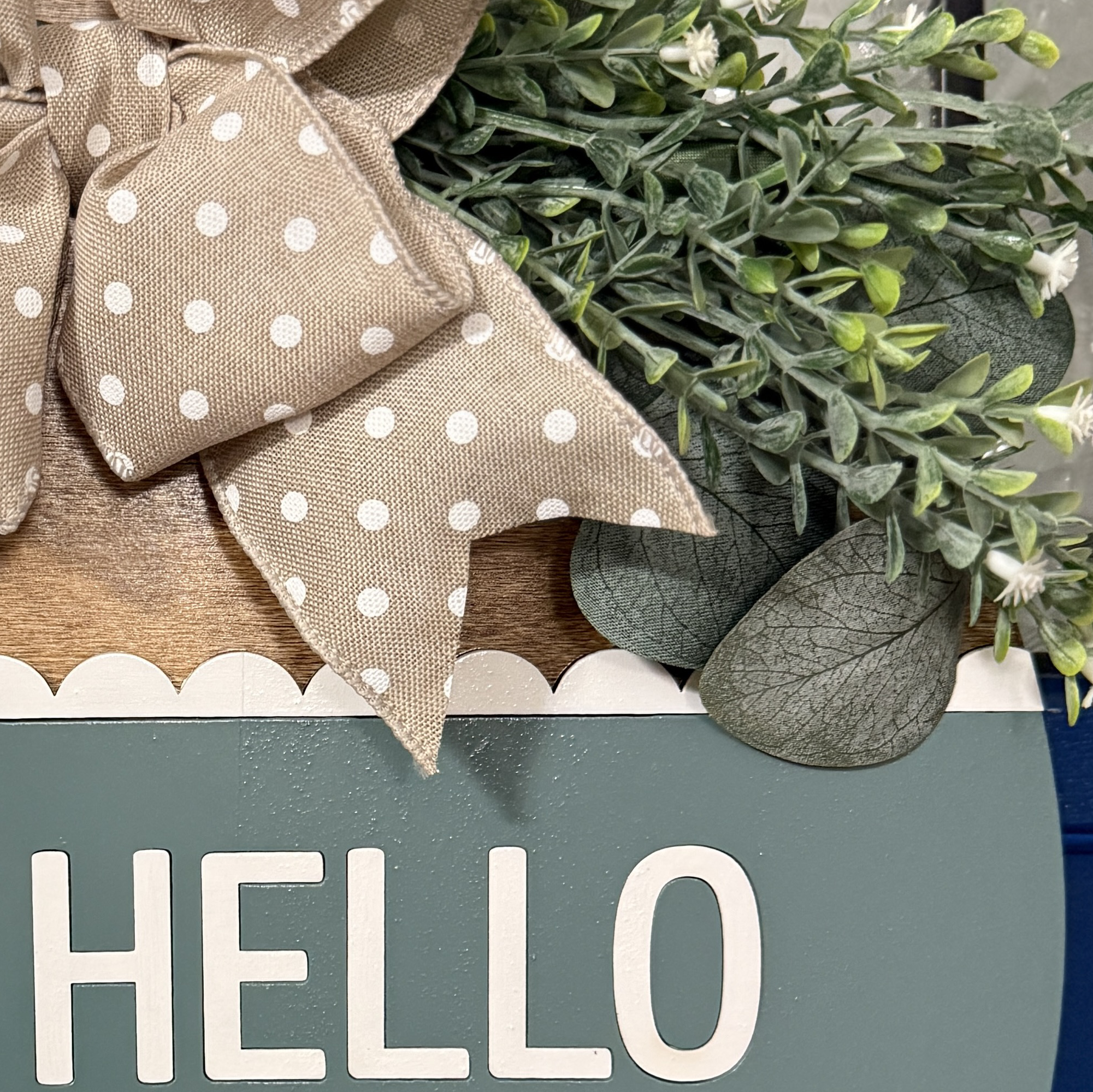 Detailed view of layered faux greenery and beige polka dot ribbon bow on spring front door decor