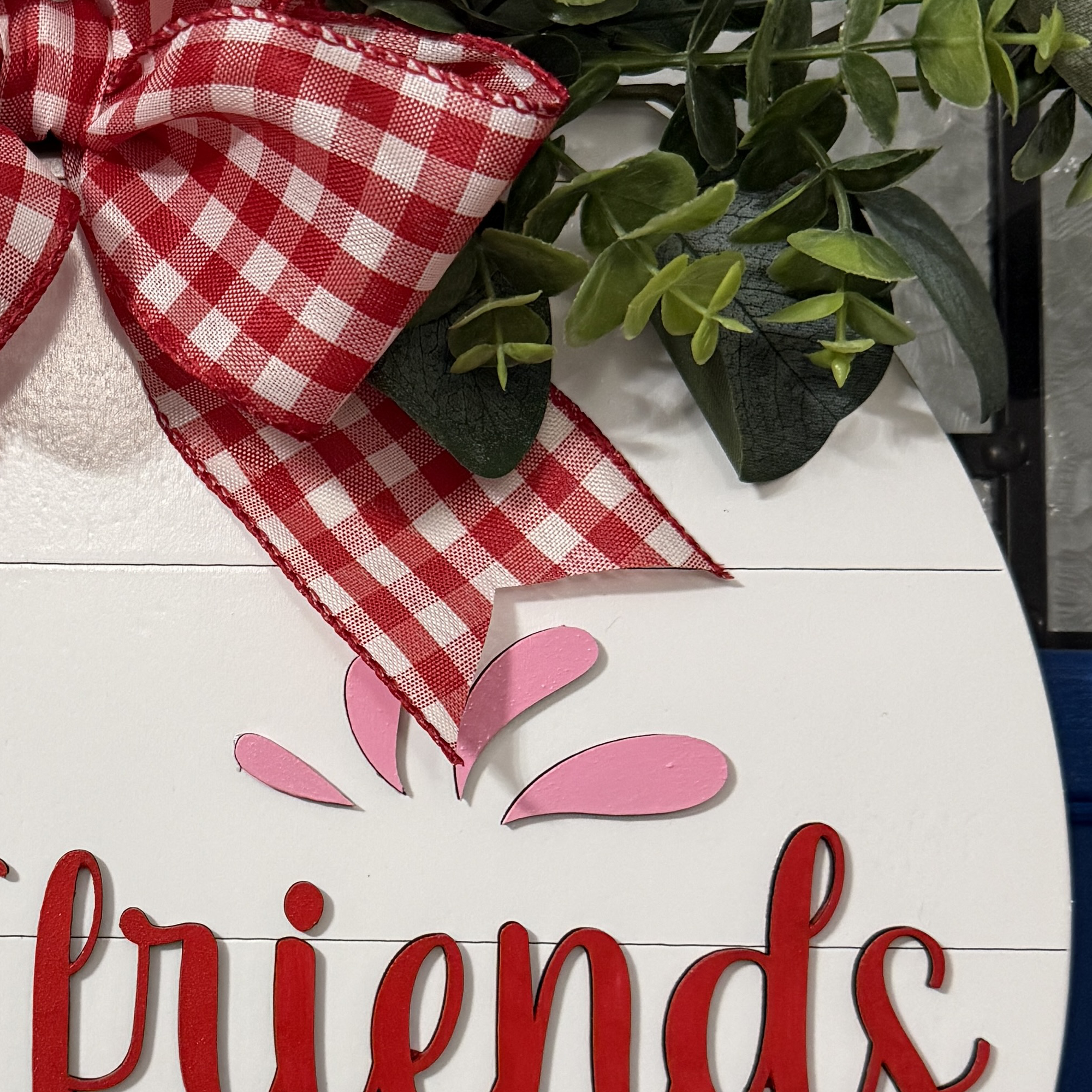 Detailed view of red gingham bow and layered greenery on top of strawberry-themed summer door decor