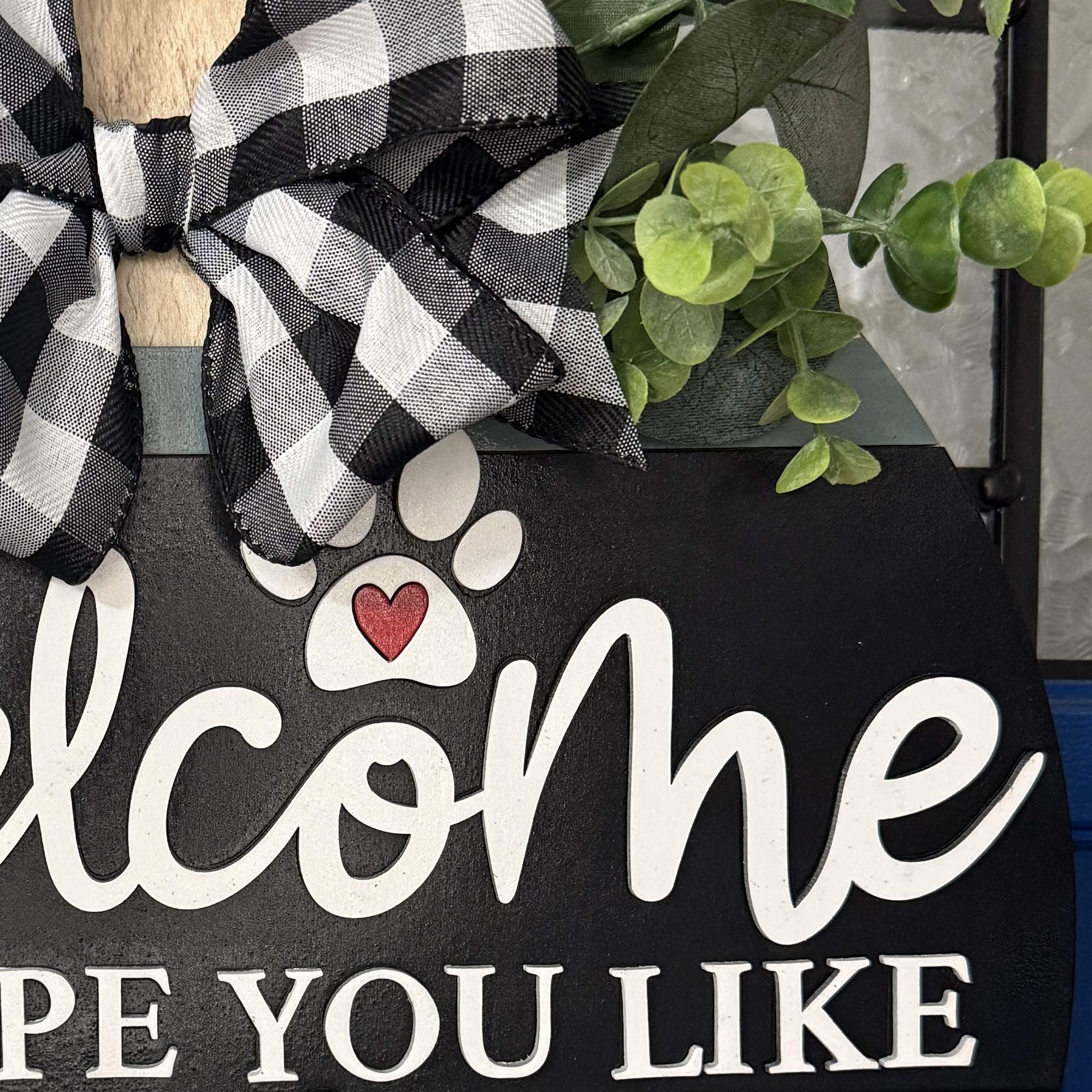 Close-up of “Welcome Hope You Like Dogs” door hanger with paw prints, heart accent, and neutral colors, hanging on a blue front door.