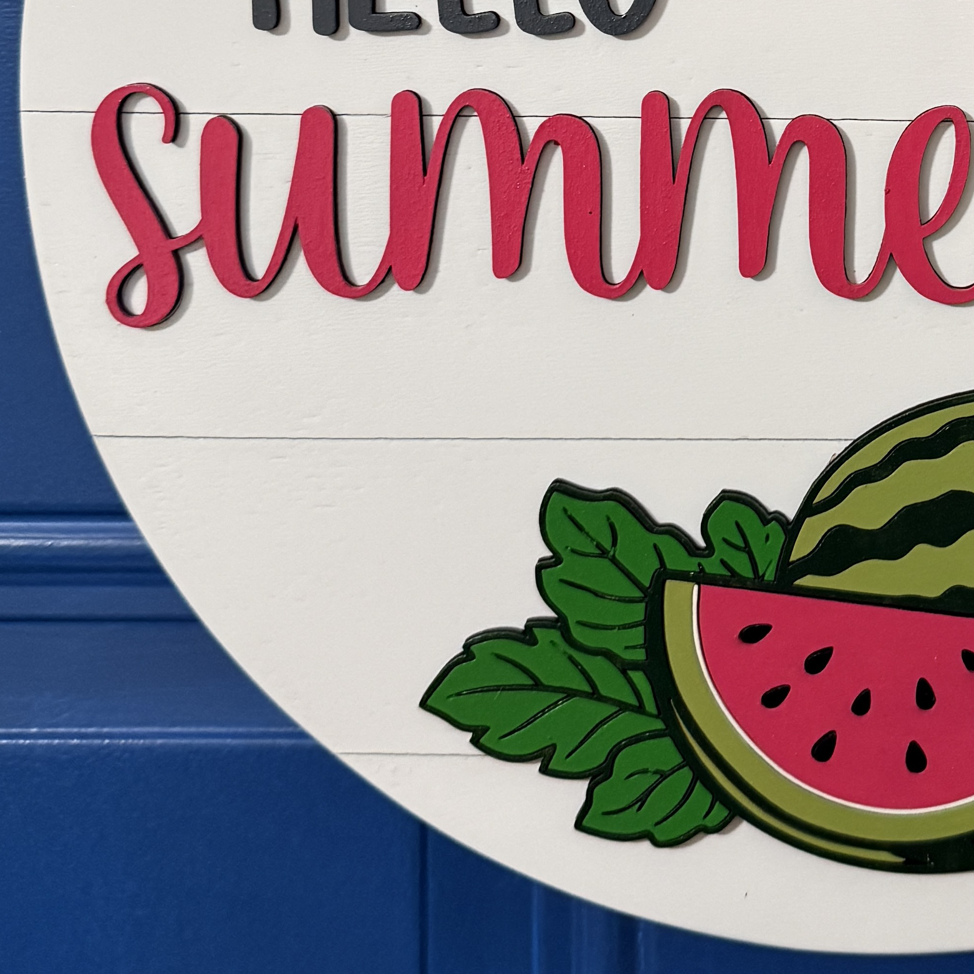 Close-up of hand-painted watermelon slice with green rind and leafy accents on round wood door hanger