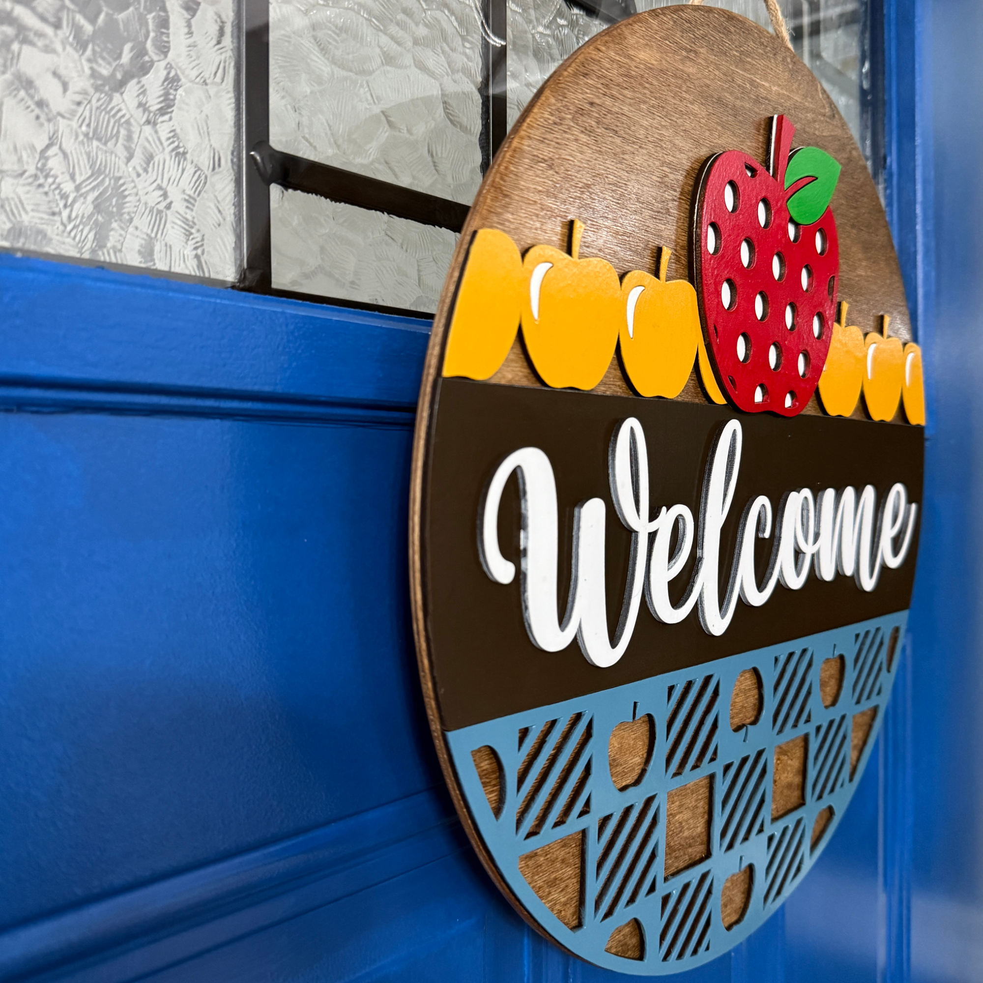 Angled side view of apple-themed welcome door hanger showing layered wood construction and depth