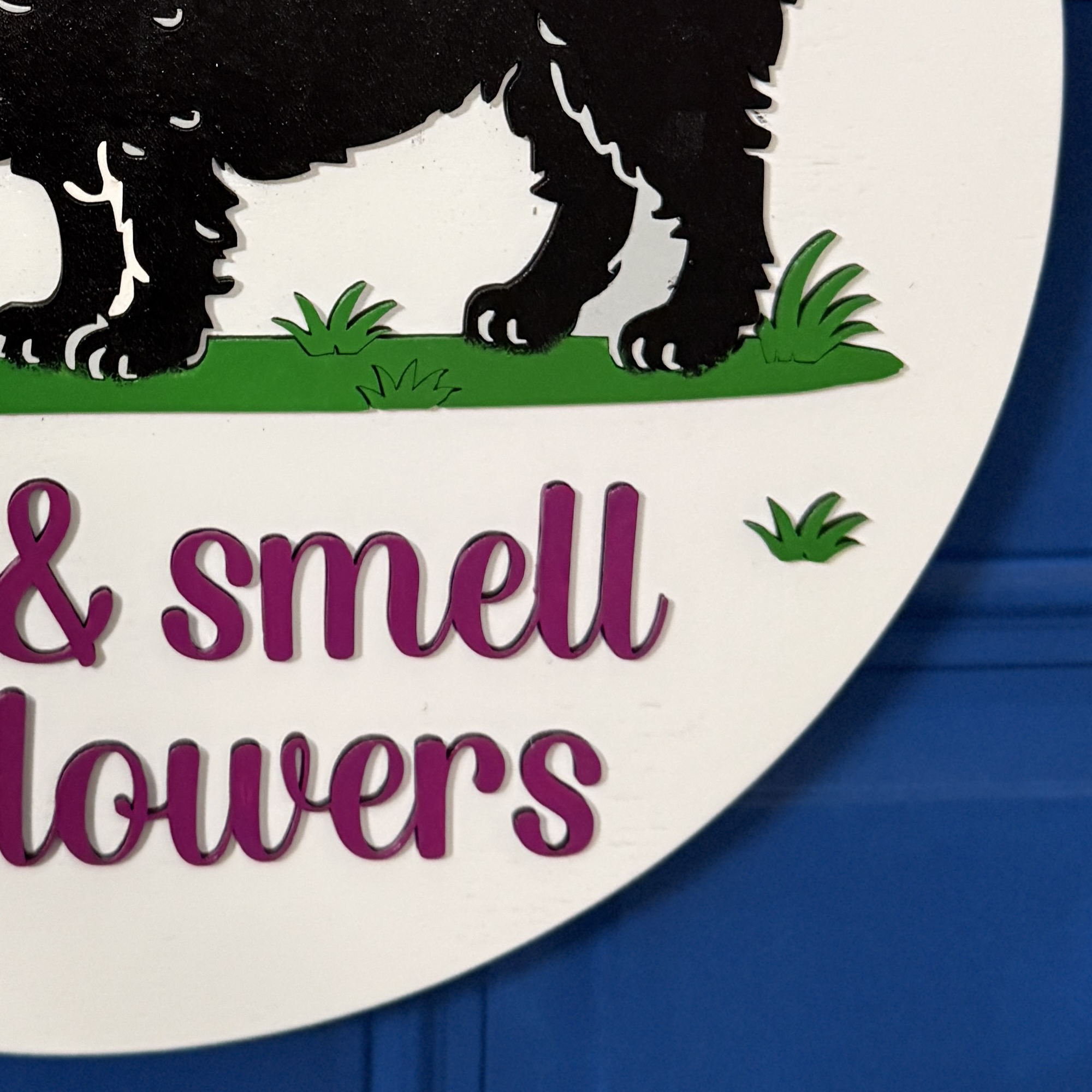 Close-up of “the flowers” raised magenta script on white round wood door hanger