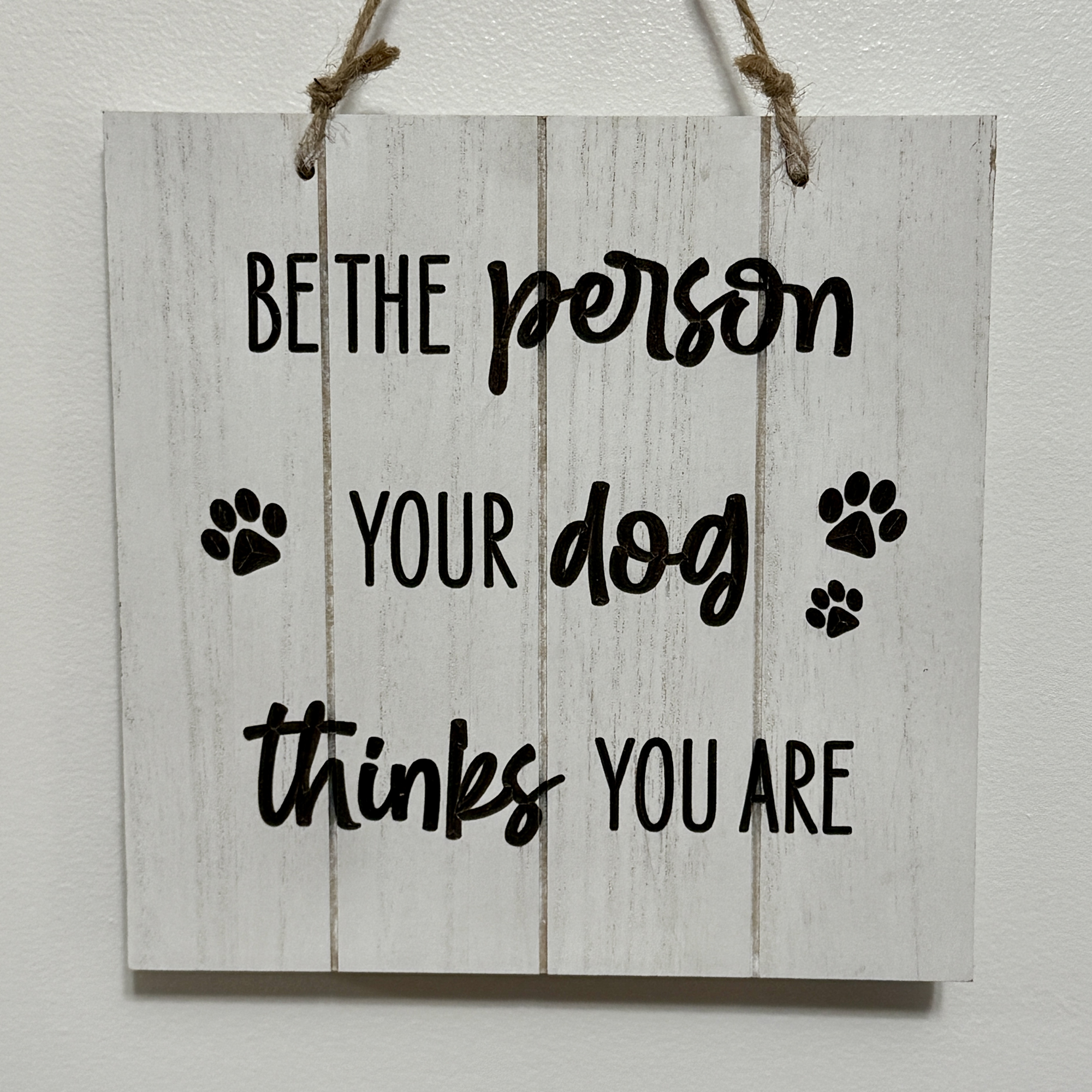 Square 8-inch farmhouse-style sign with black paw prints and quote “Be the person your dog thinks you are” on white shiplap background