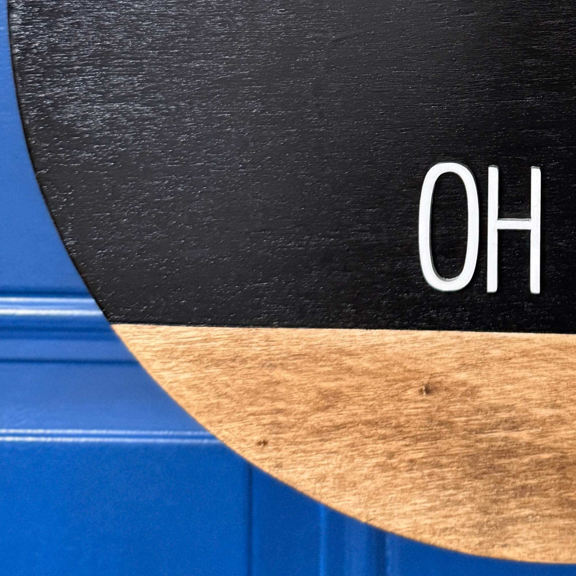 Close-up of white oh hey lettering on black painted wood door hanger with natural stained wood accent