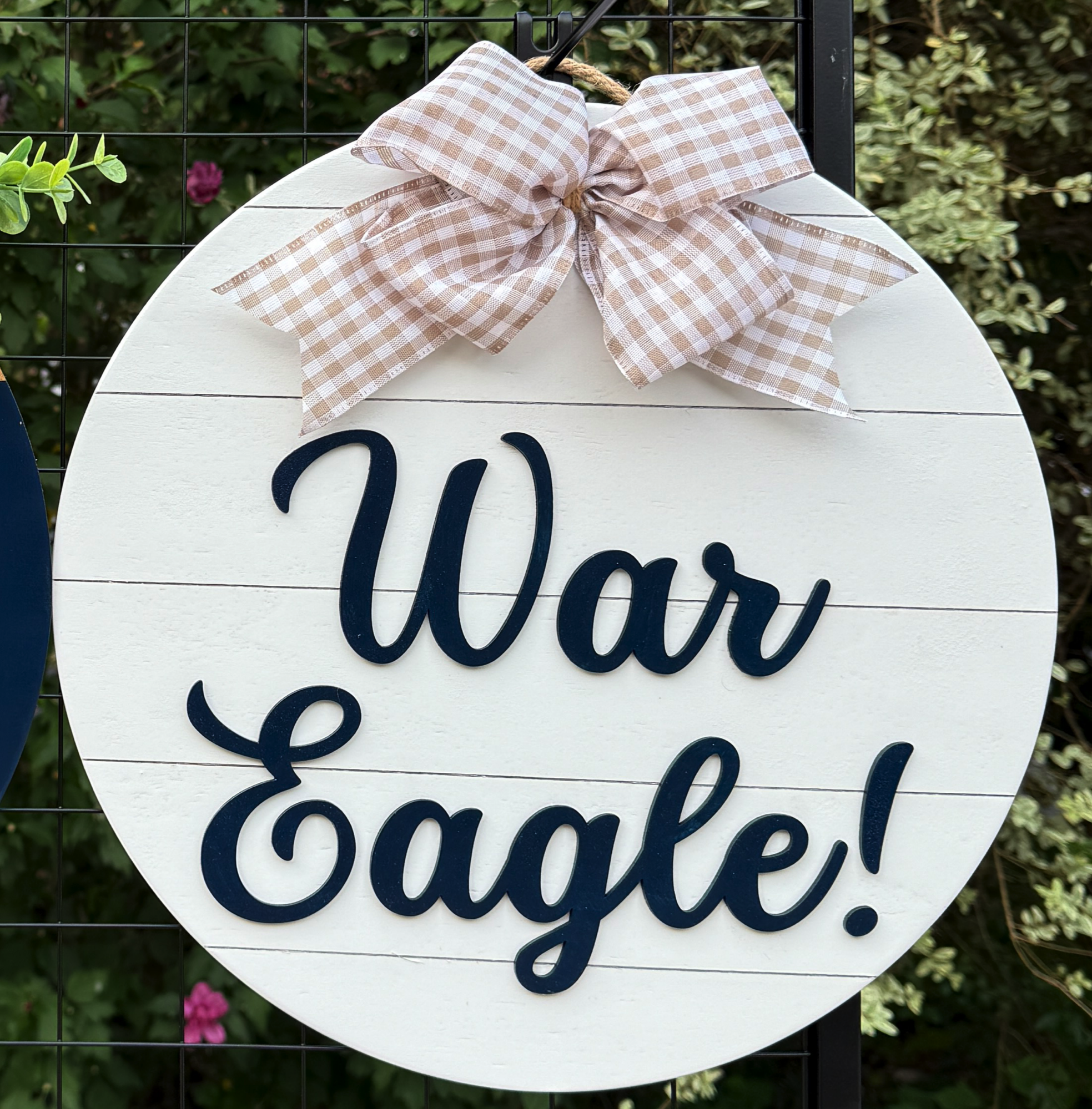 Round War Eagle door hanger with bold navy script on white shiplap background and beige gingham bow