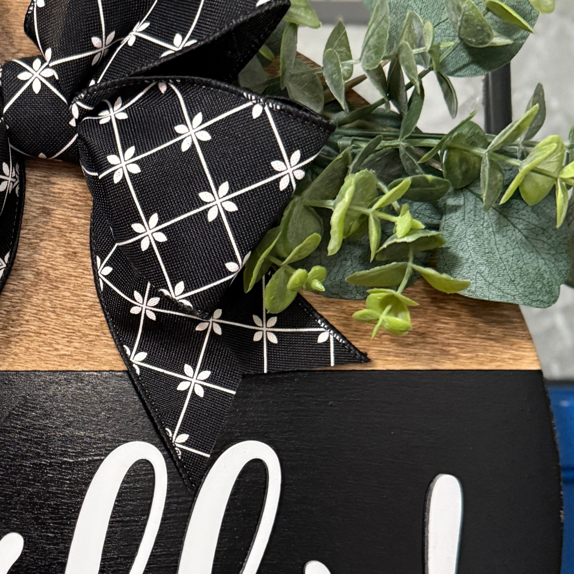 Detailed view of black ribbon bow and faux greenery on handcrafted round wooden Hello sign