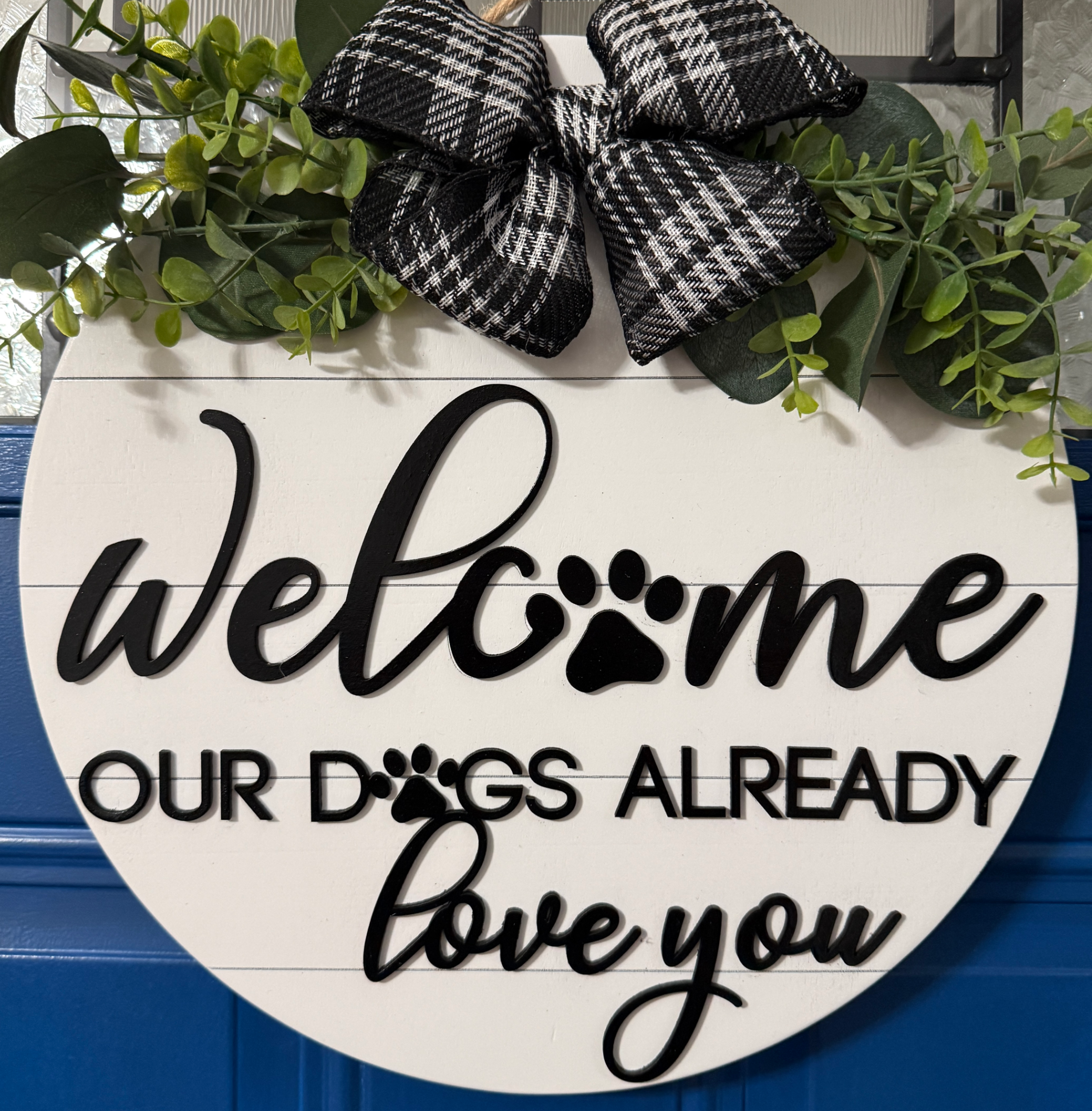 Full view of round white welcome sign with paw print detail and “our dogs already loves you” message