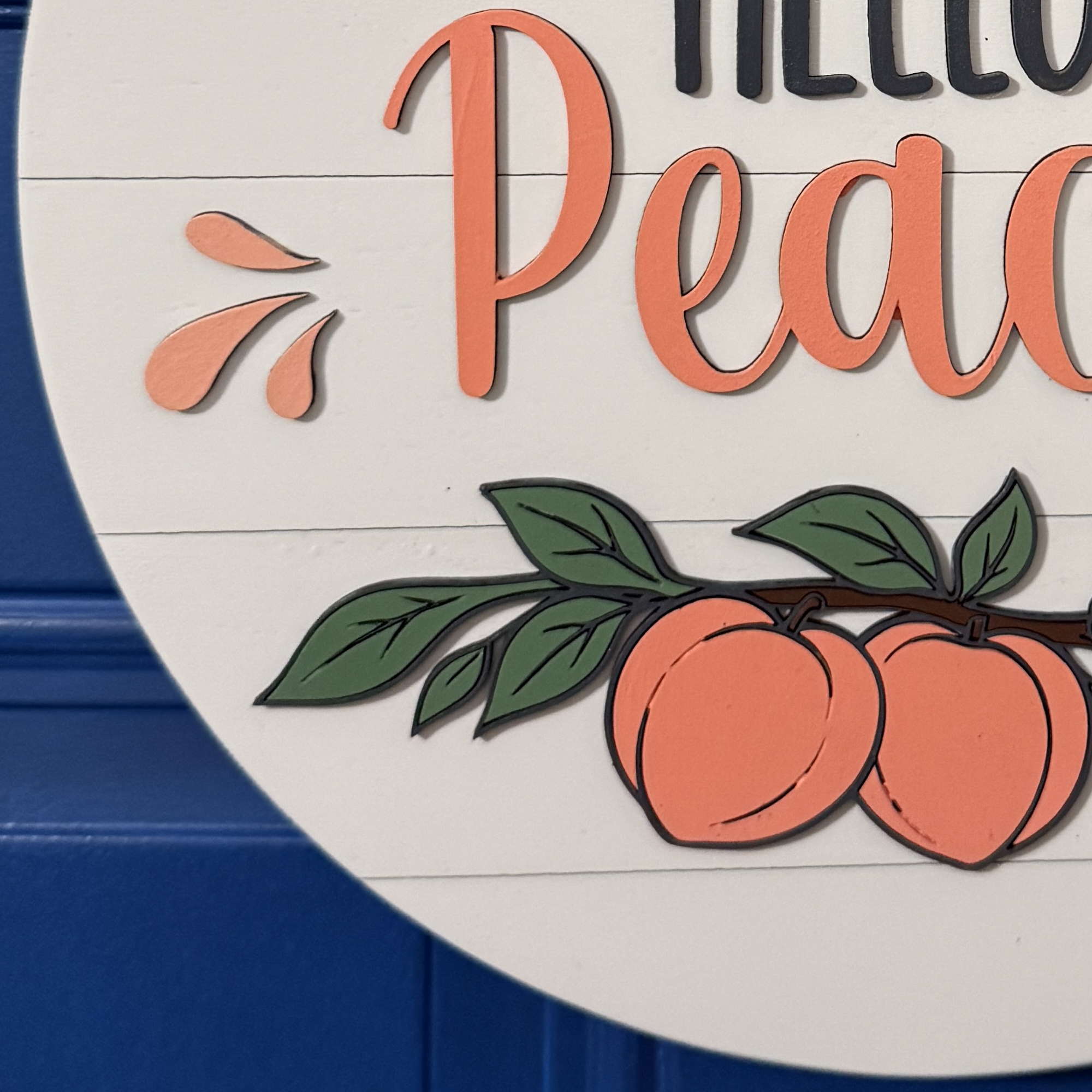 Detailed view of hand-painted peaches with green leaves and blossoms on round wood door hanger
