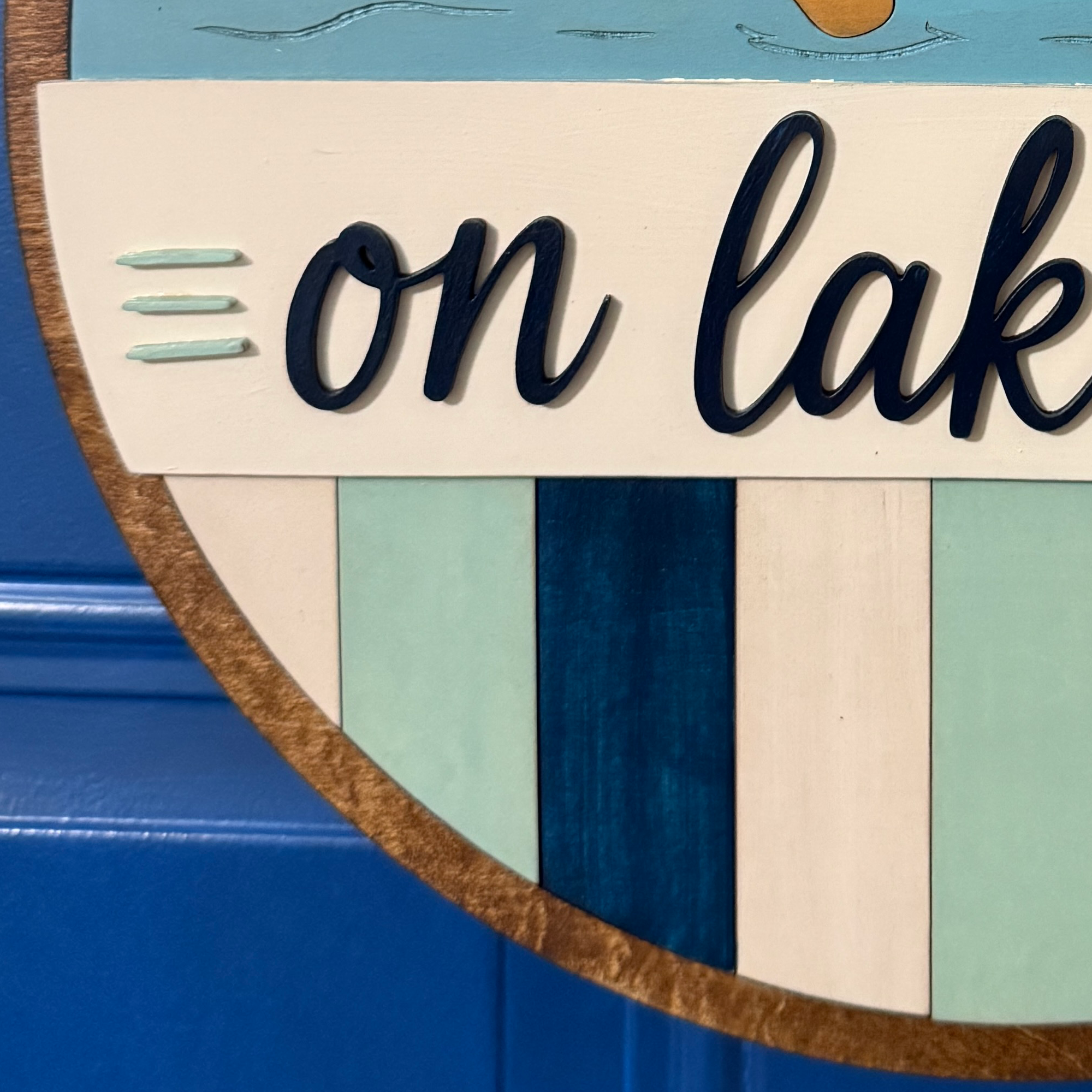 Close-up of raised "On Lake Time" script lettering over blue striped wood accents.