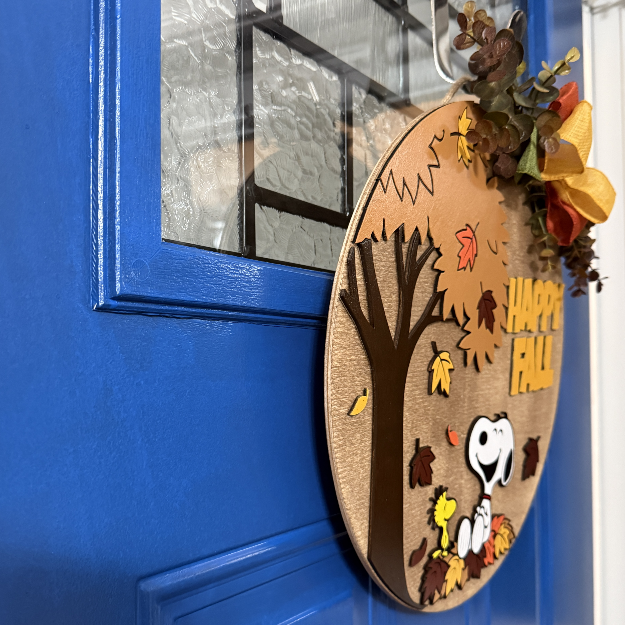 Side view of Happy Fall door hanger showing layered design and decorative bow with greenery