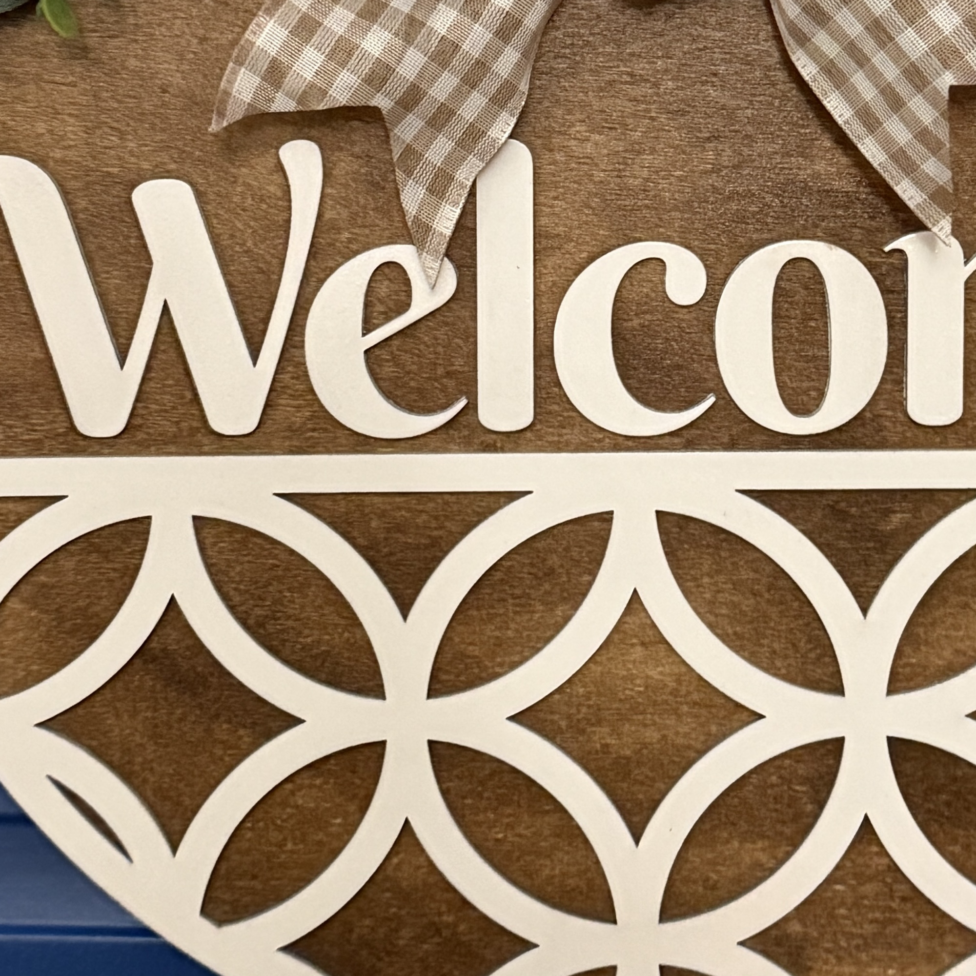 Close-up of layered wood design showing “Welcome” script and cutout pattern details