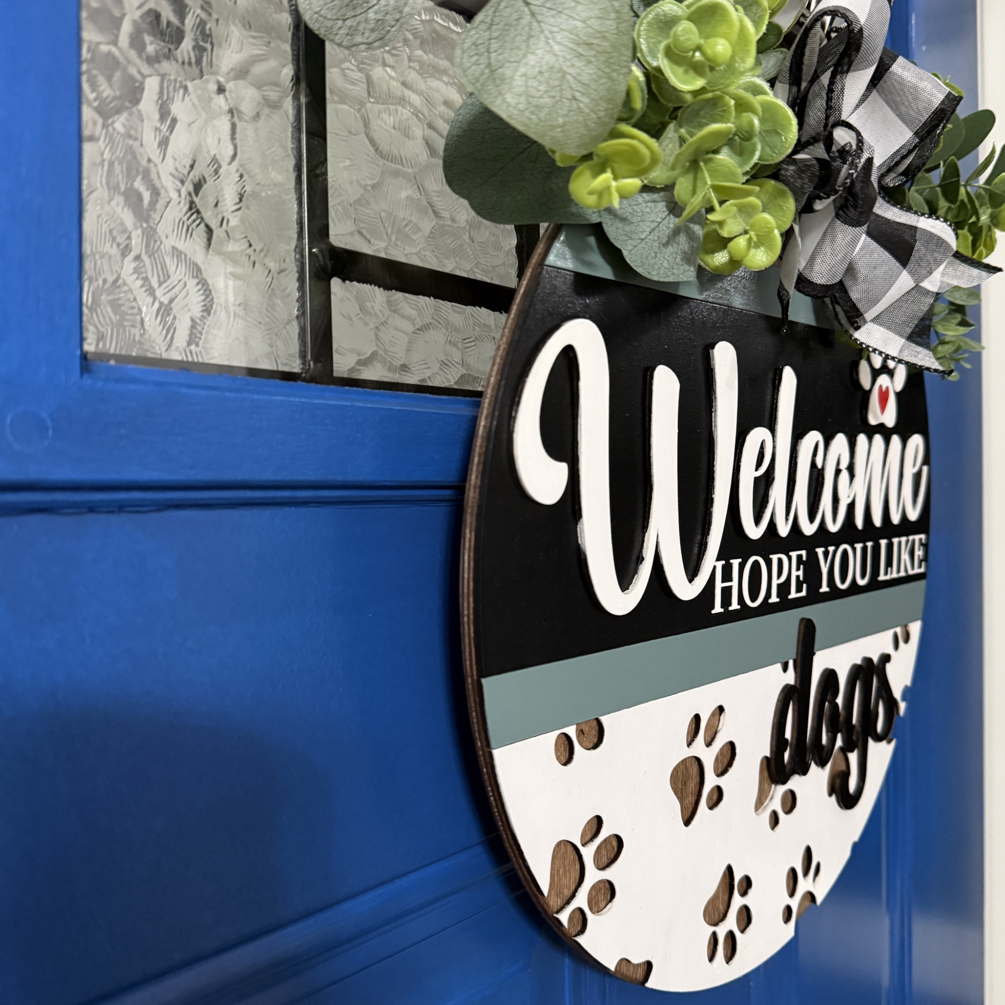 Angled side view of round dog welcome sign showing layered wood design and greenery accent