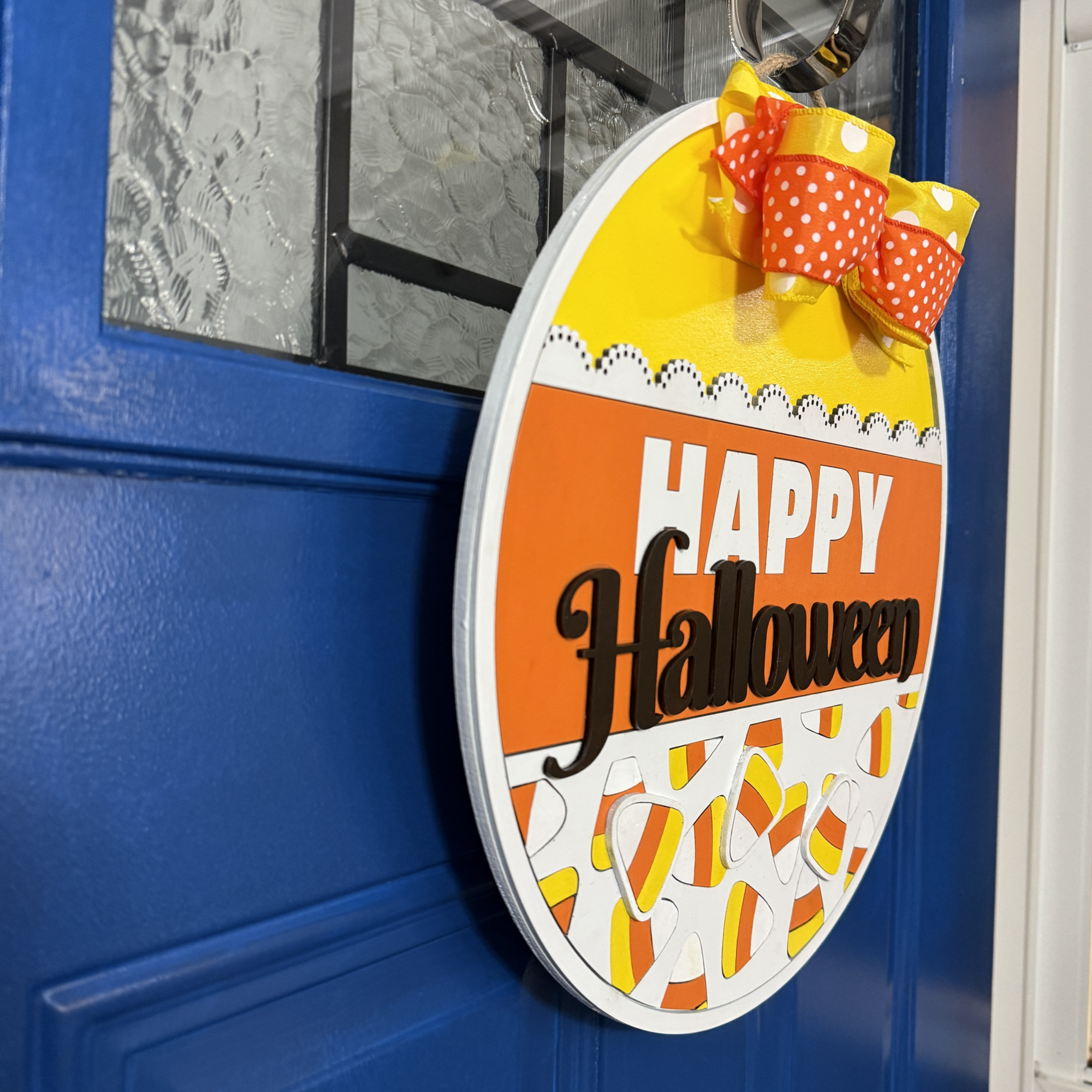 Side angle of Halloween candy corn door hanger with bow, hanging on a blue front door