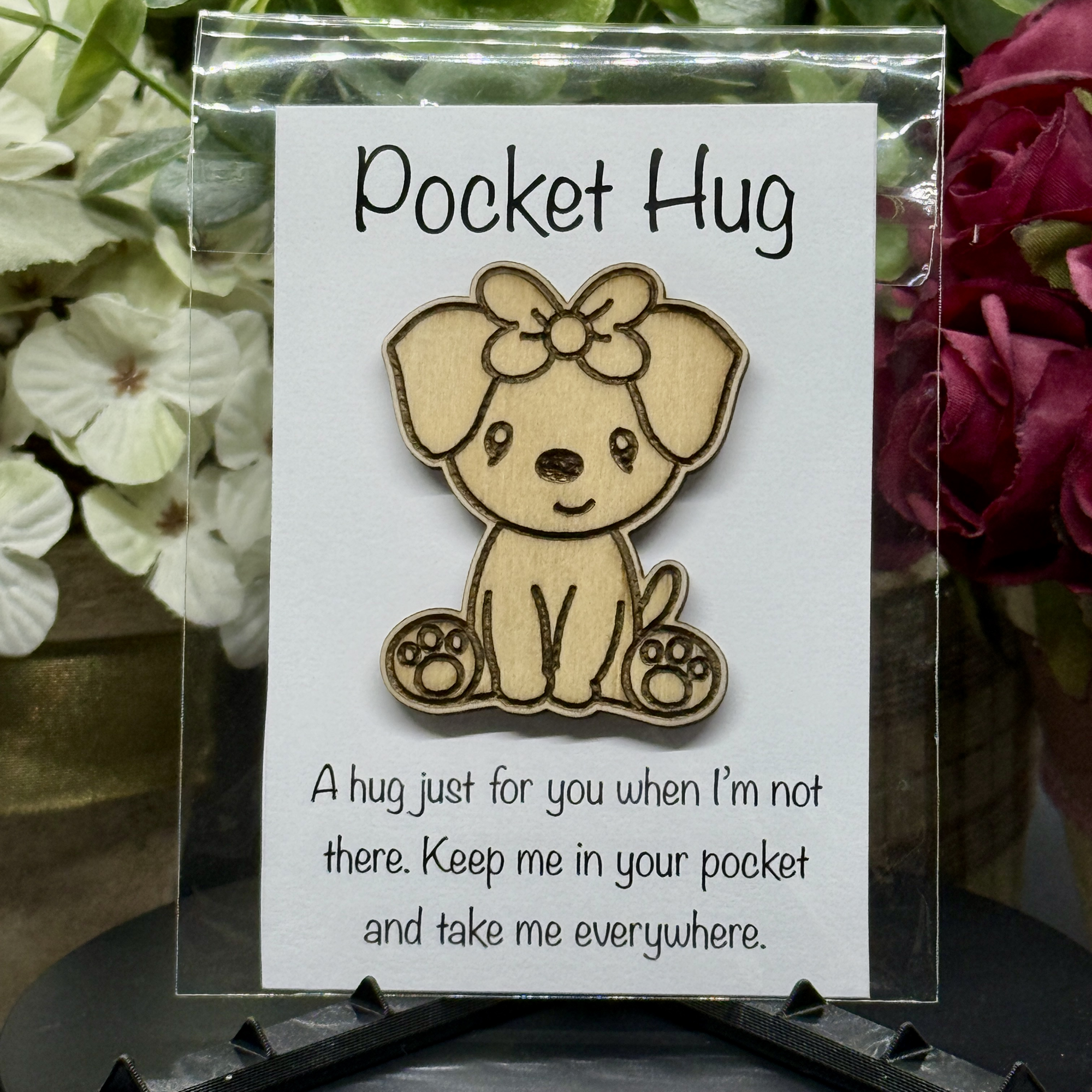 Bow Pup Pocket Hug token on printed card with white and magenta floral background – laser-cut wood dog with bow on head