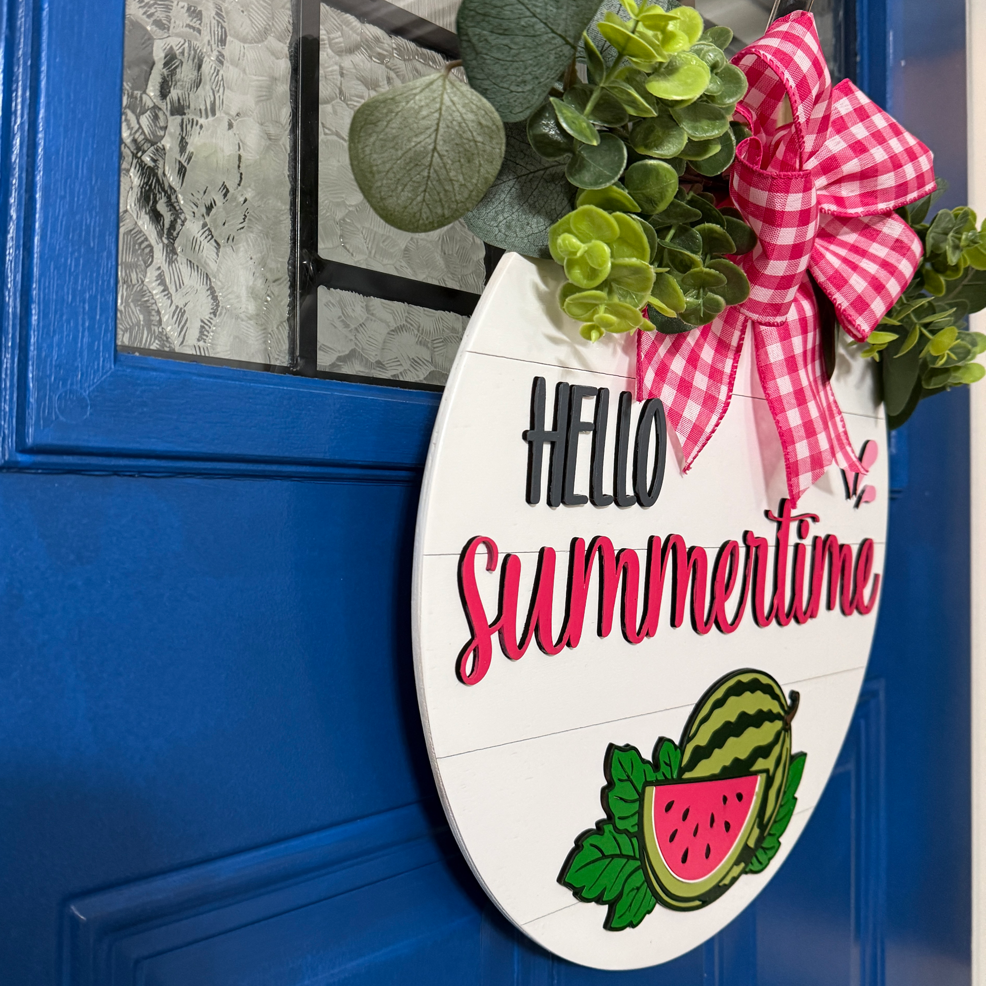 Angled side view of Hello Summertime round wood door hanger showing layered thickness, greenery, and dimensional lettering