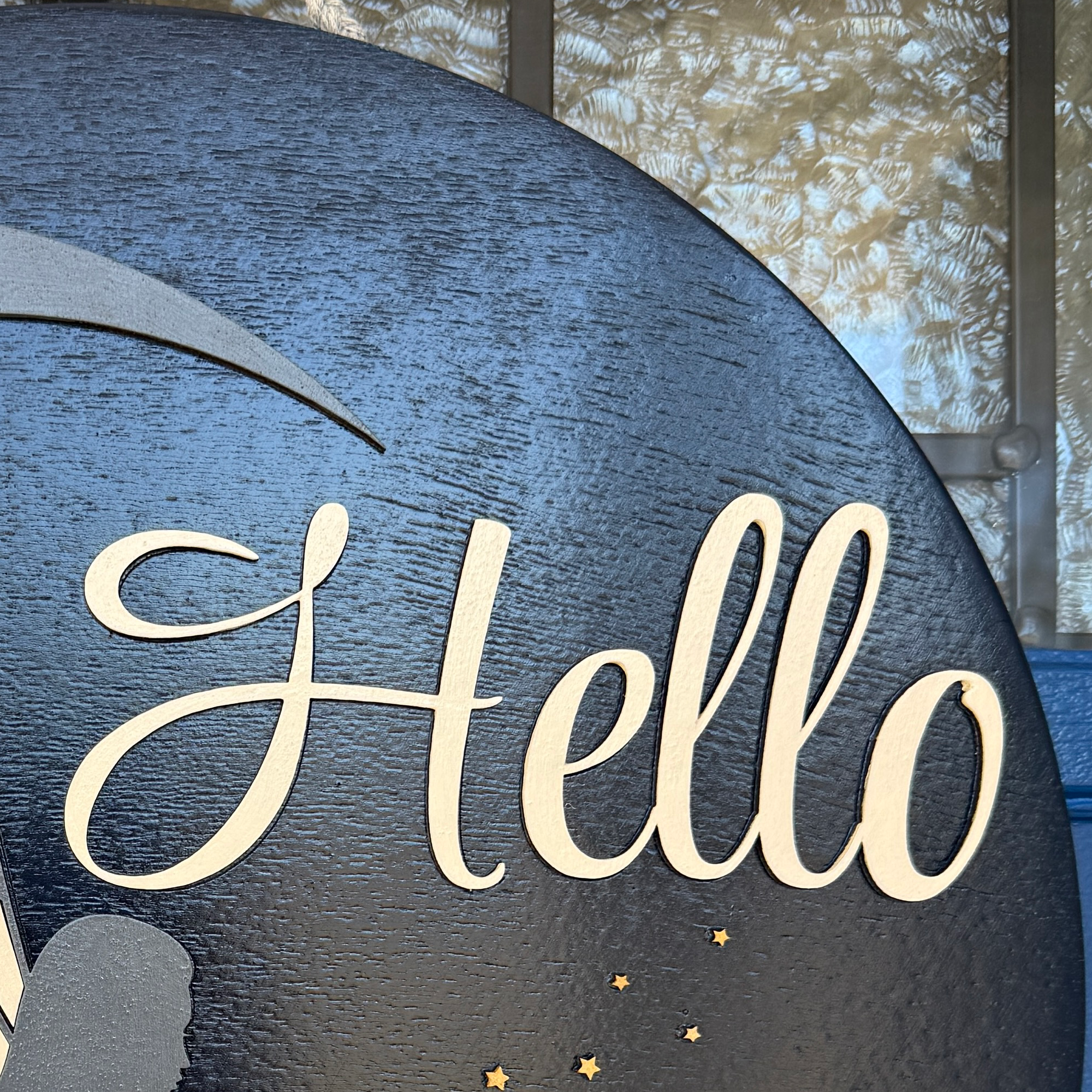 Close-up of gold hello script lettering on black fairy moon wood door hanger