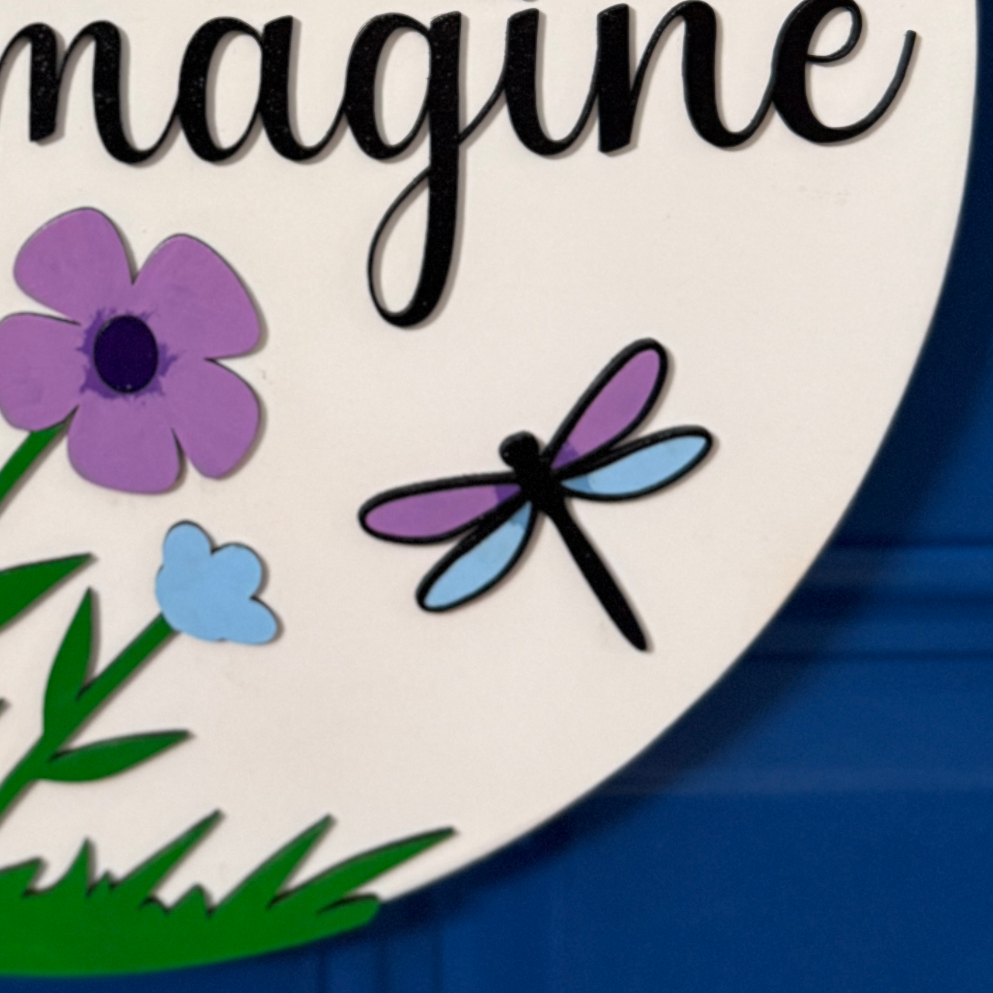 Close-up of “imagine” script lettering in black on floral spring door hanger