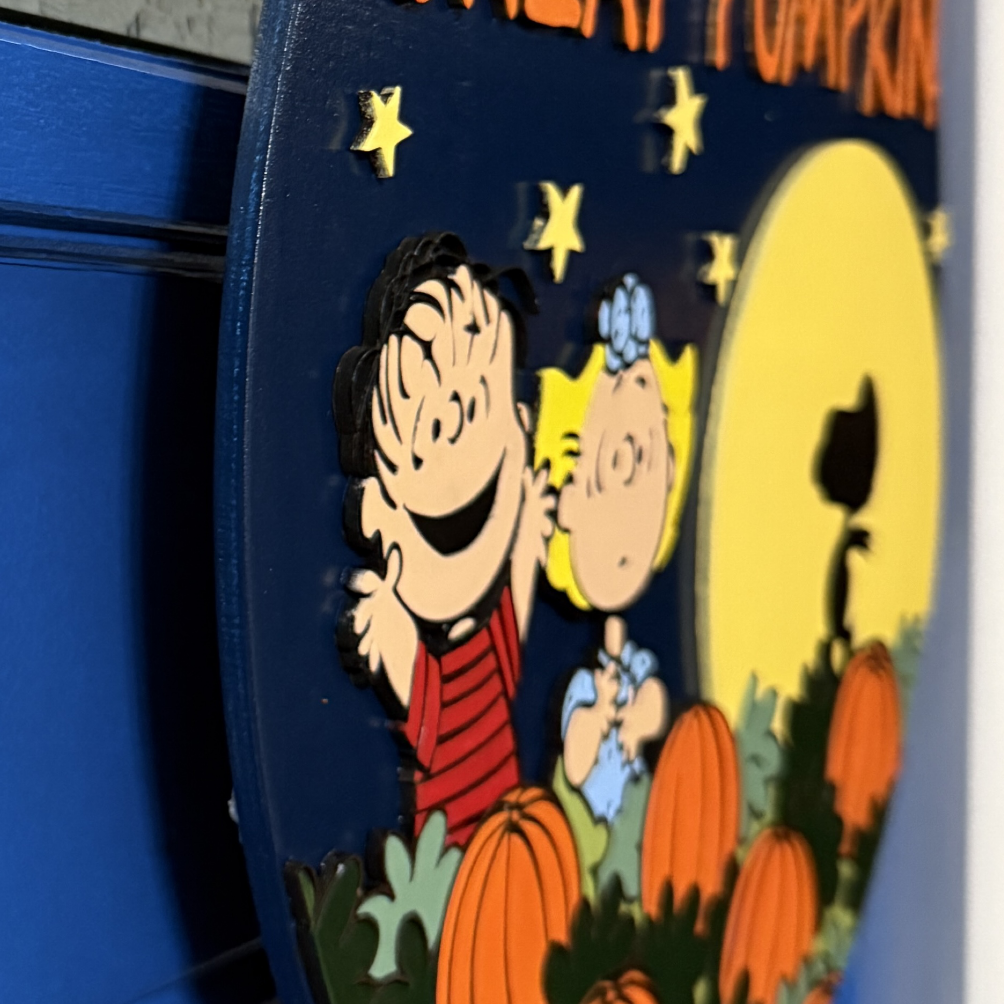 Close-up of Peanuts characters Linus and Sally among pumpkins with stars and Snoopy’s moonlit silhouette