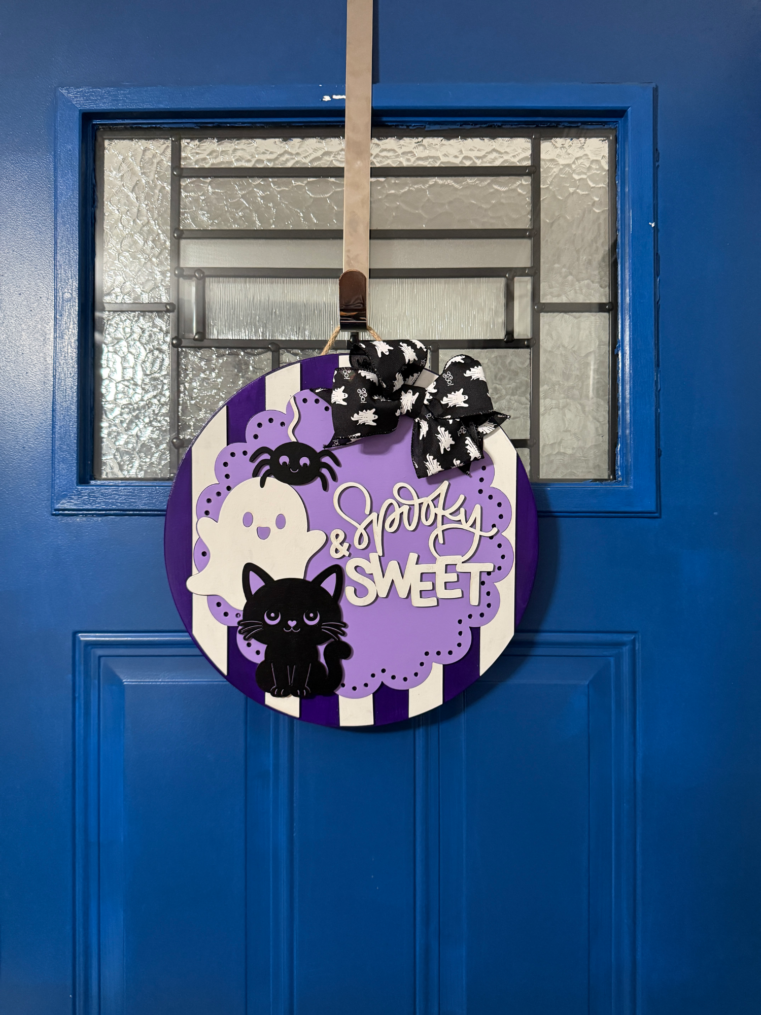 Spooky and Sweet purple Halloween door hanger displayed on a bright blue front door with layered ghosts, black cat, and bow