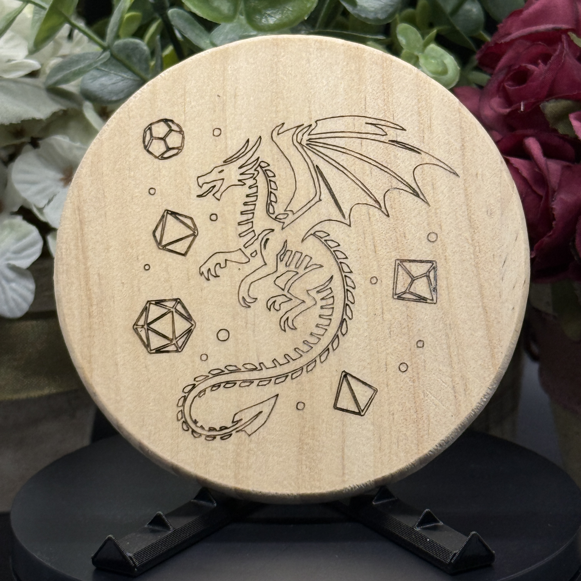 Round pine wood coaster with playful engraved dragon surrounded by polyhedral dice, perfect for tabletop gamers and fantasy lovers