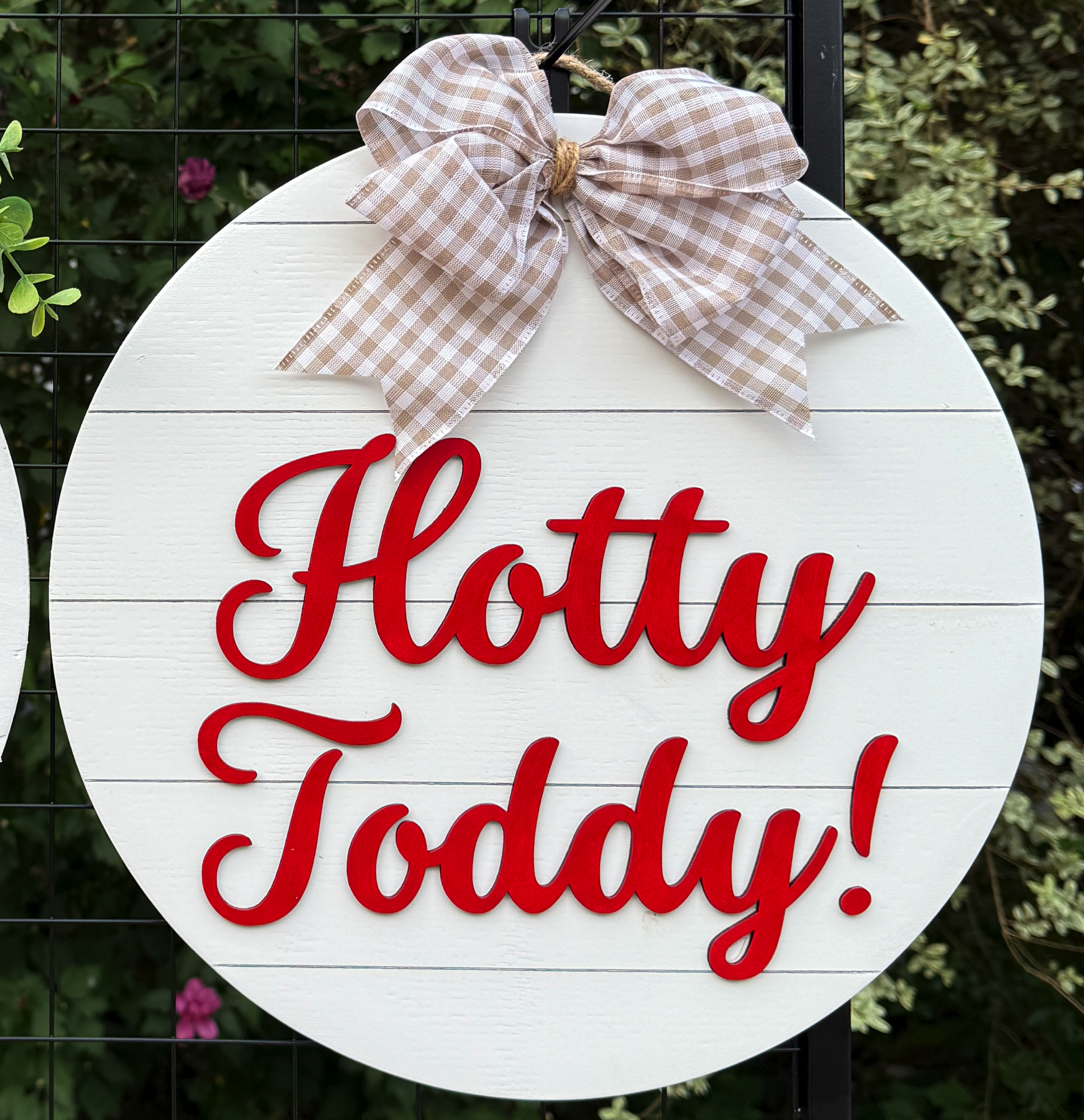 Round Hotty Toddy door hanger with bold red script on white shiplap background and beige gingham bow