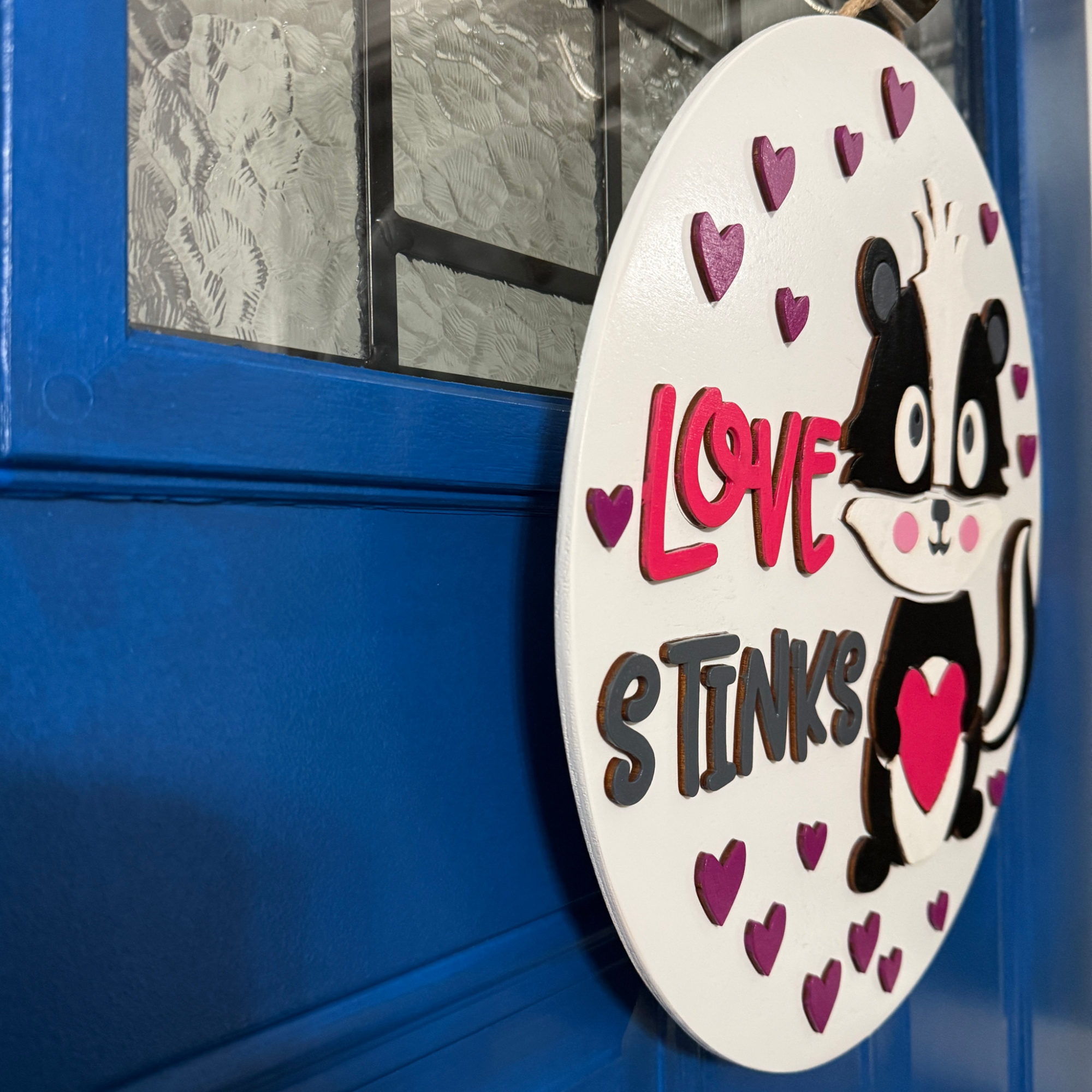Angled view of Love Stinks skunk door hanger showing dimensional layered wood construction