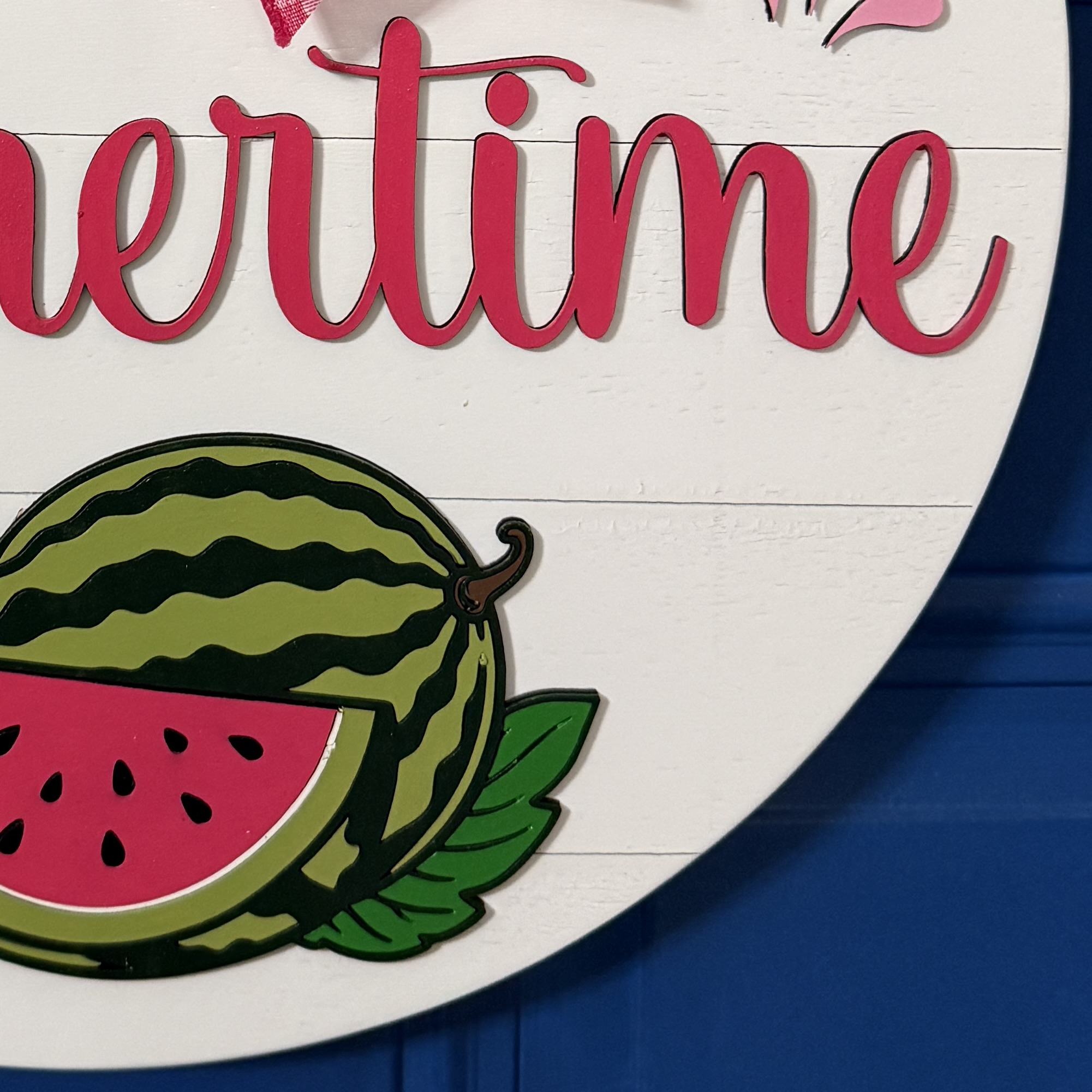 Detailed view of bright pink watermelon slice with black seeds and green leaves along bottom of door hanger