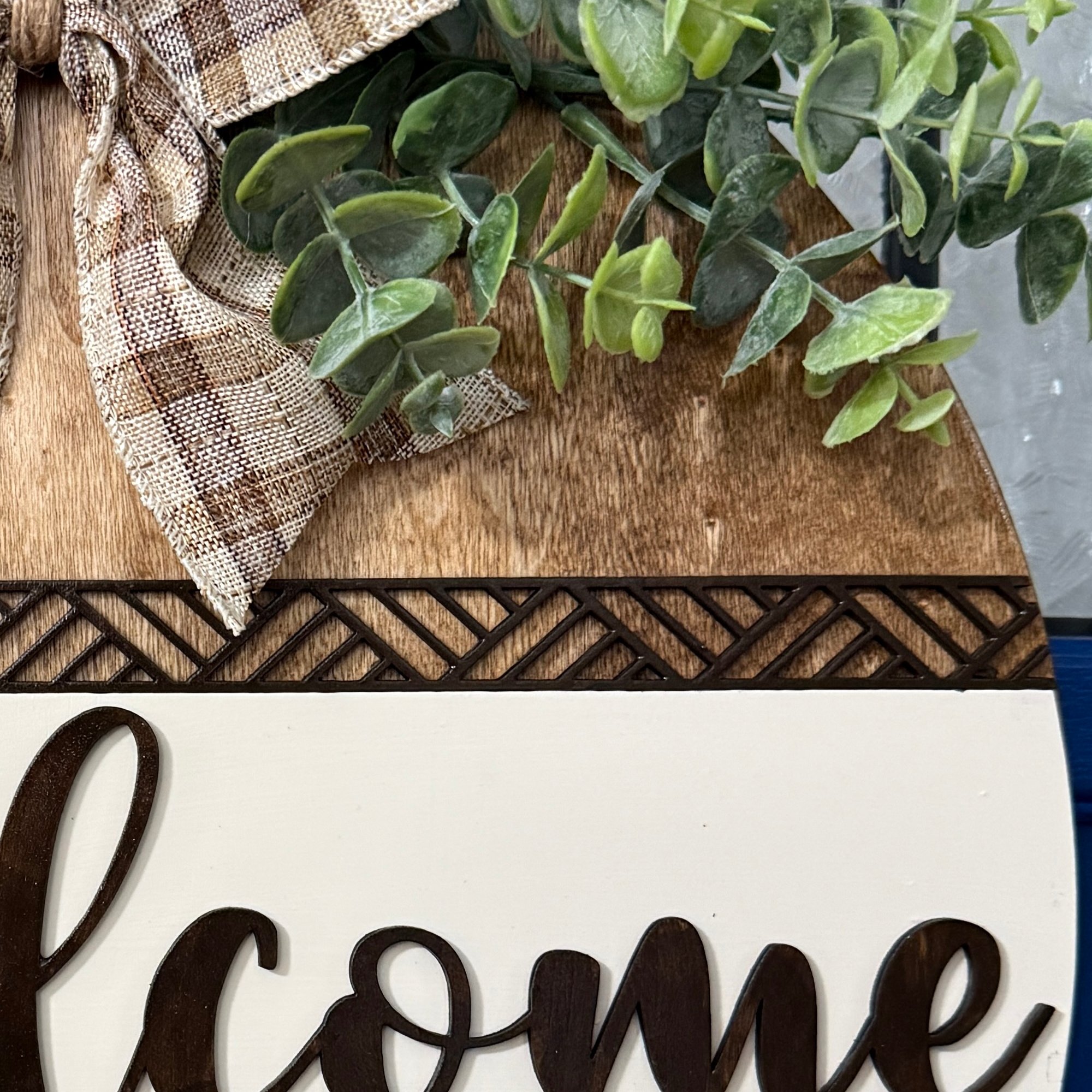 Close-up of greenery and plaid bow at top of rustic wood door hanger