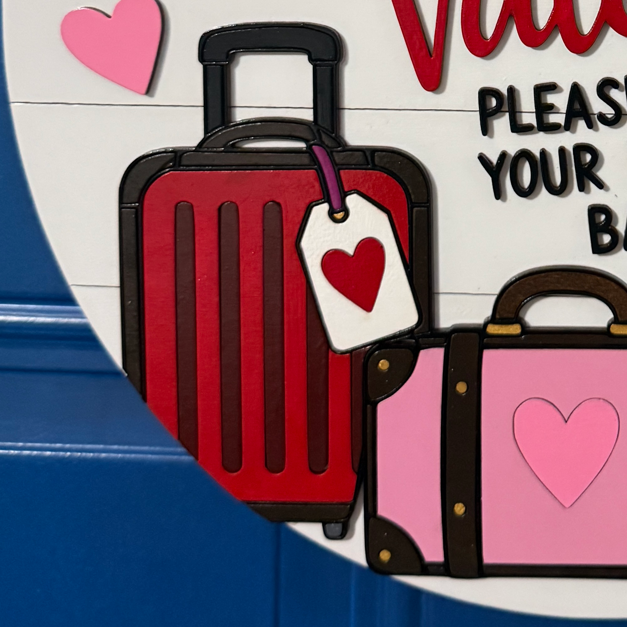 Close-up of layered red and pink suitcases with heart luggage tags on Valentine door hanger