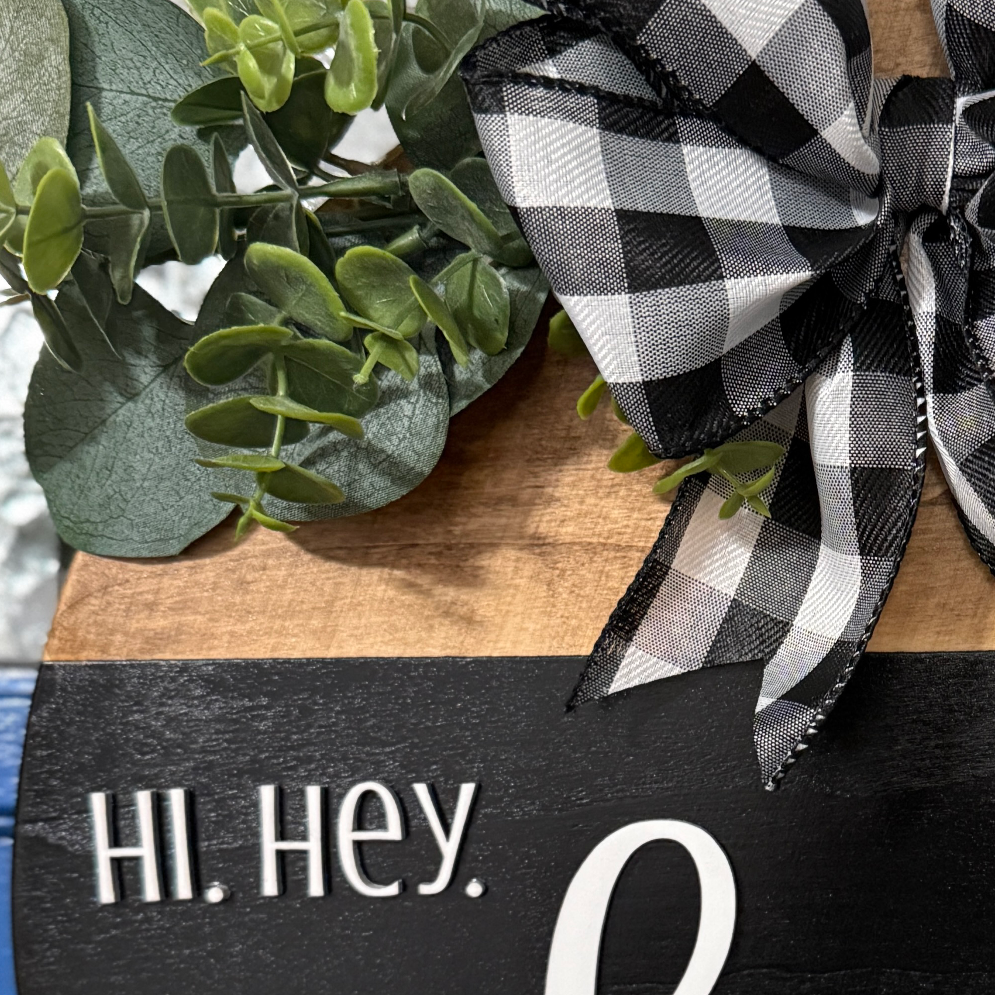 Close-up of greenery and black buffalo plaid bow attached to handcrafted hello wood door hanger