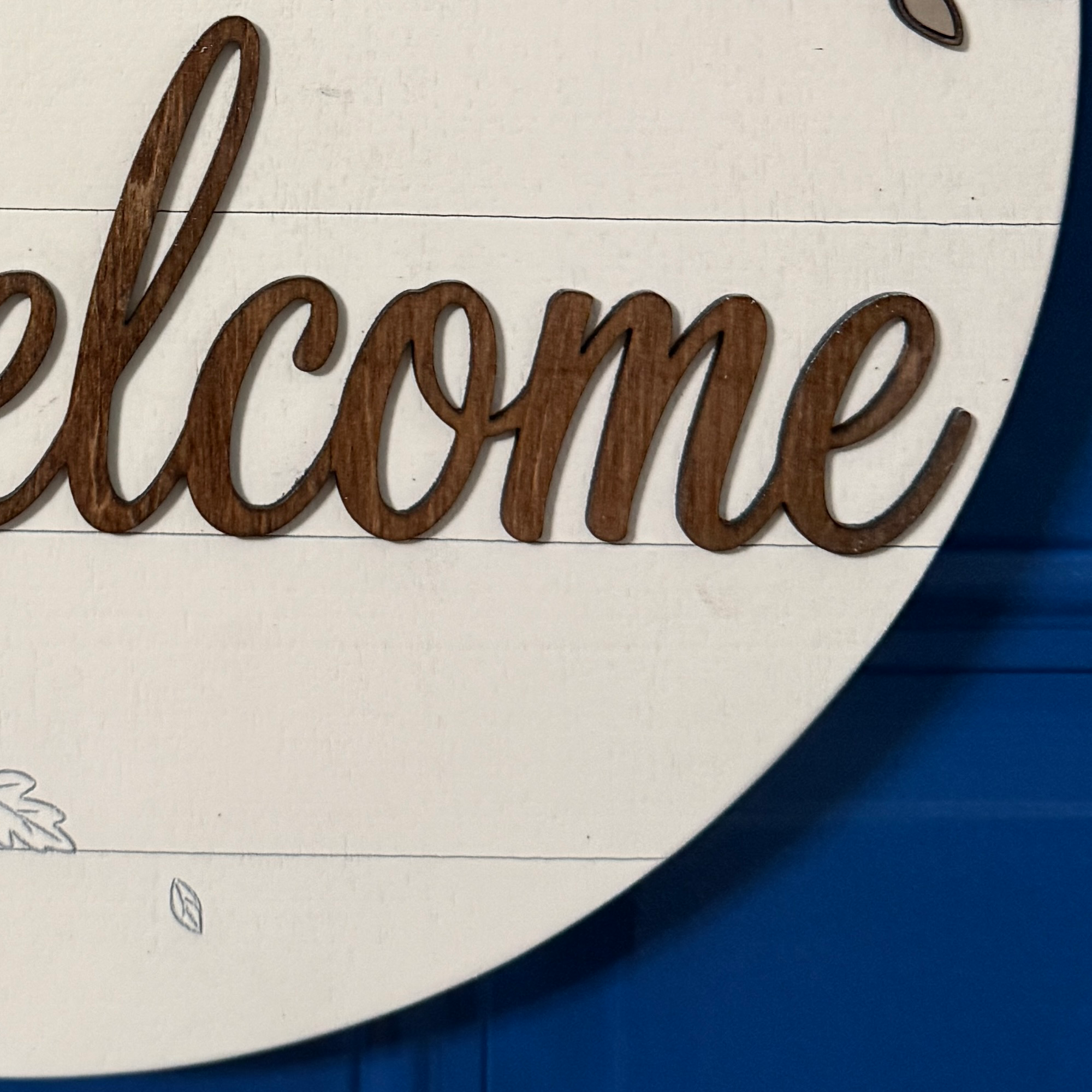 Close-up of Welcome lettering and delicate engraved falling leaf details along bottom of fall door hanger
