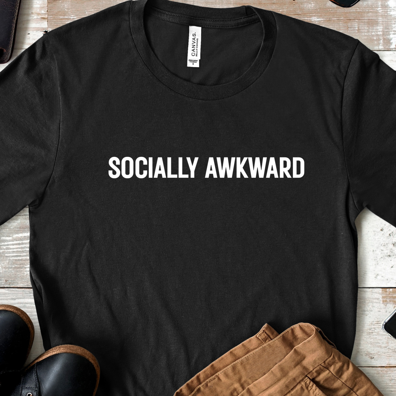 Flat lay of black socially awkward graphic t shirt with centered white text on wooden background