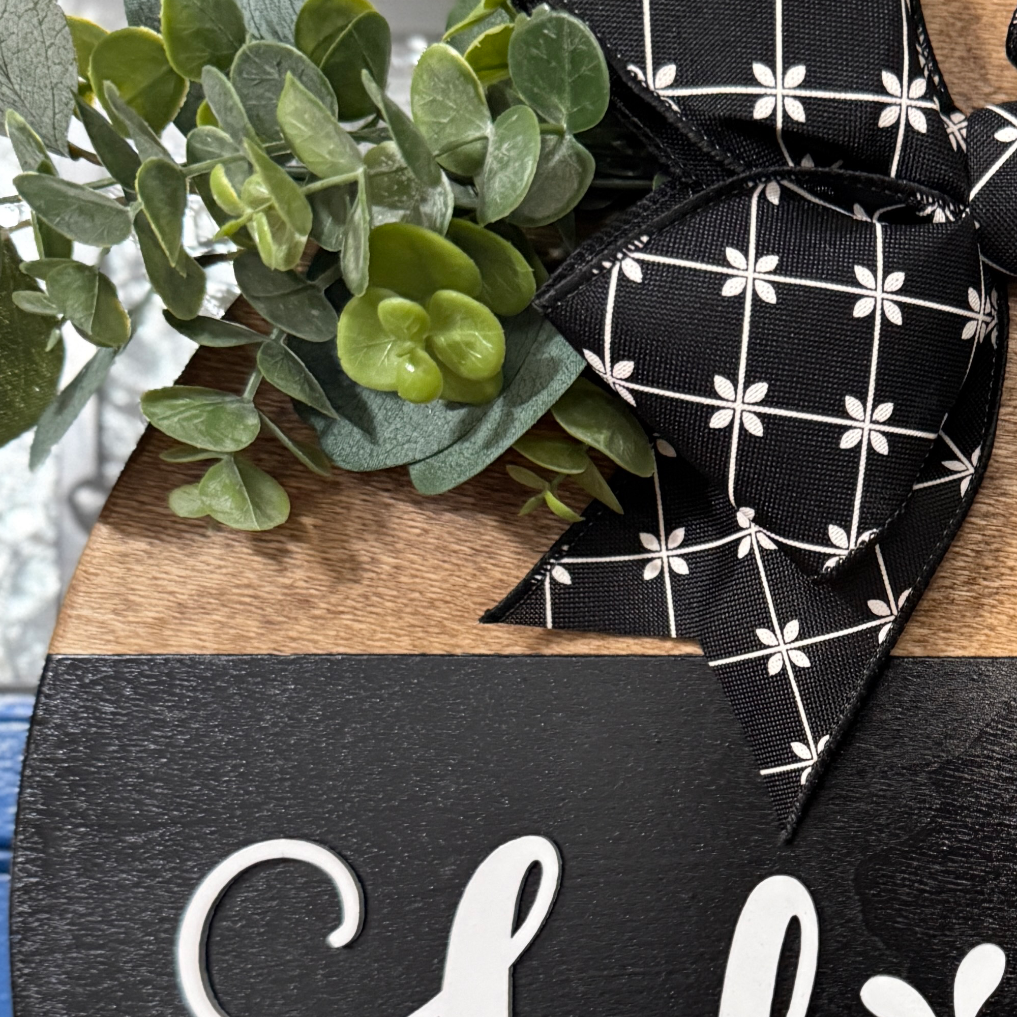 Close-up of greenery and black patterned bow attached to rustic wood Hello door hanger