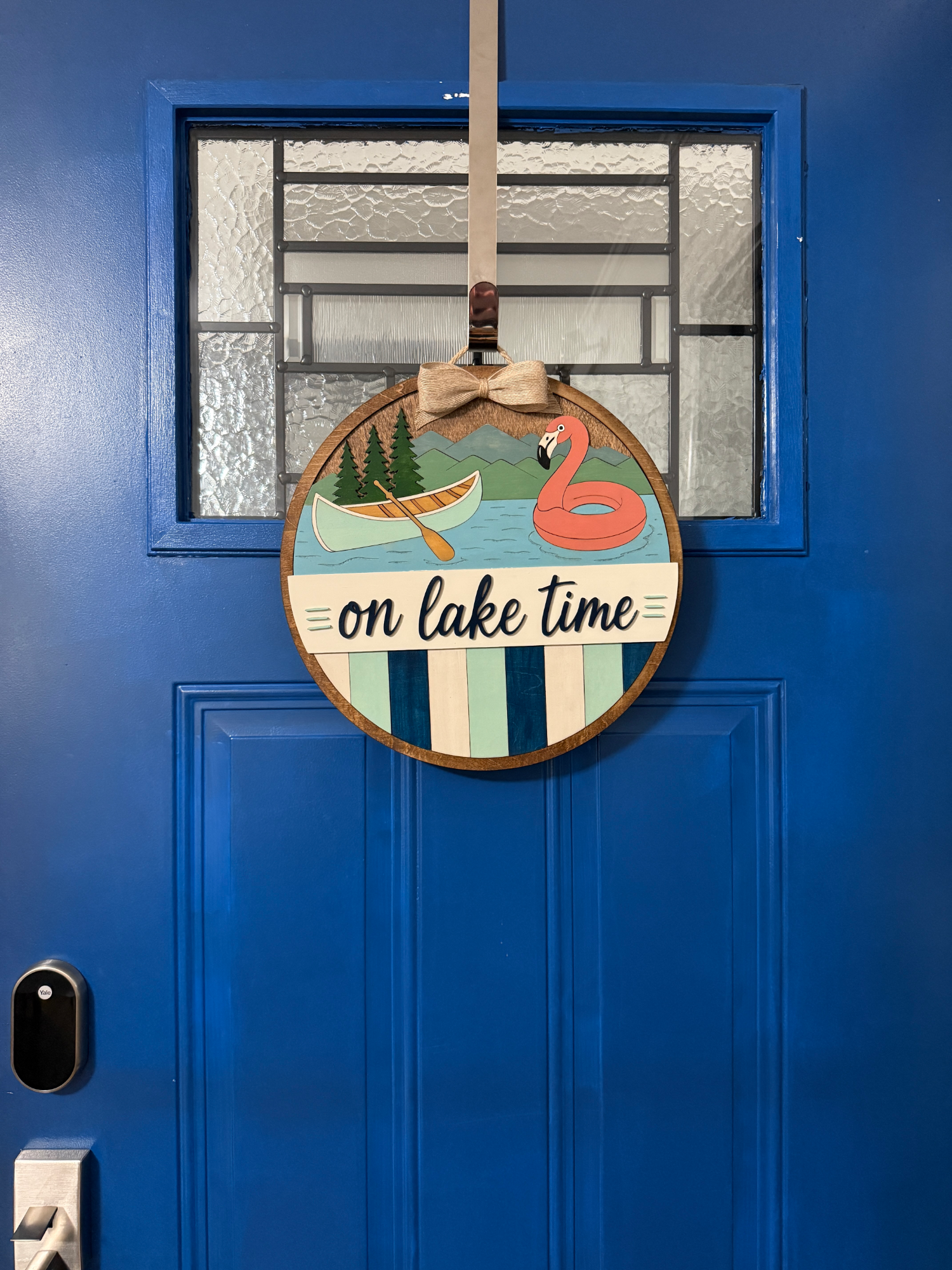 On Lake Time lakehouse door hanger displayed on a bright blue front door.